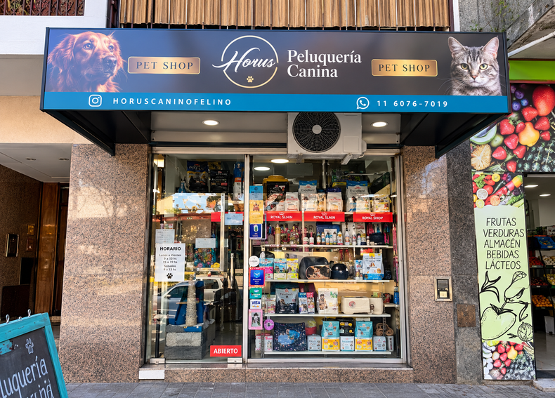 Fachada de una tienda de mascotas con un letrero azul, escaparates y estantes con artículos para mascotas en el interior