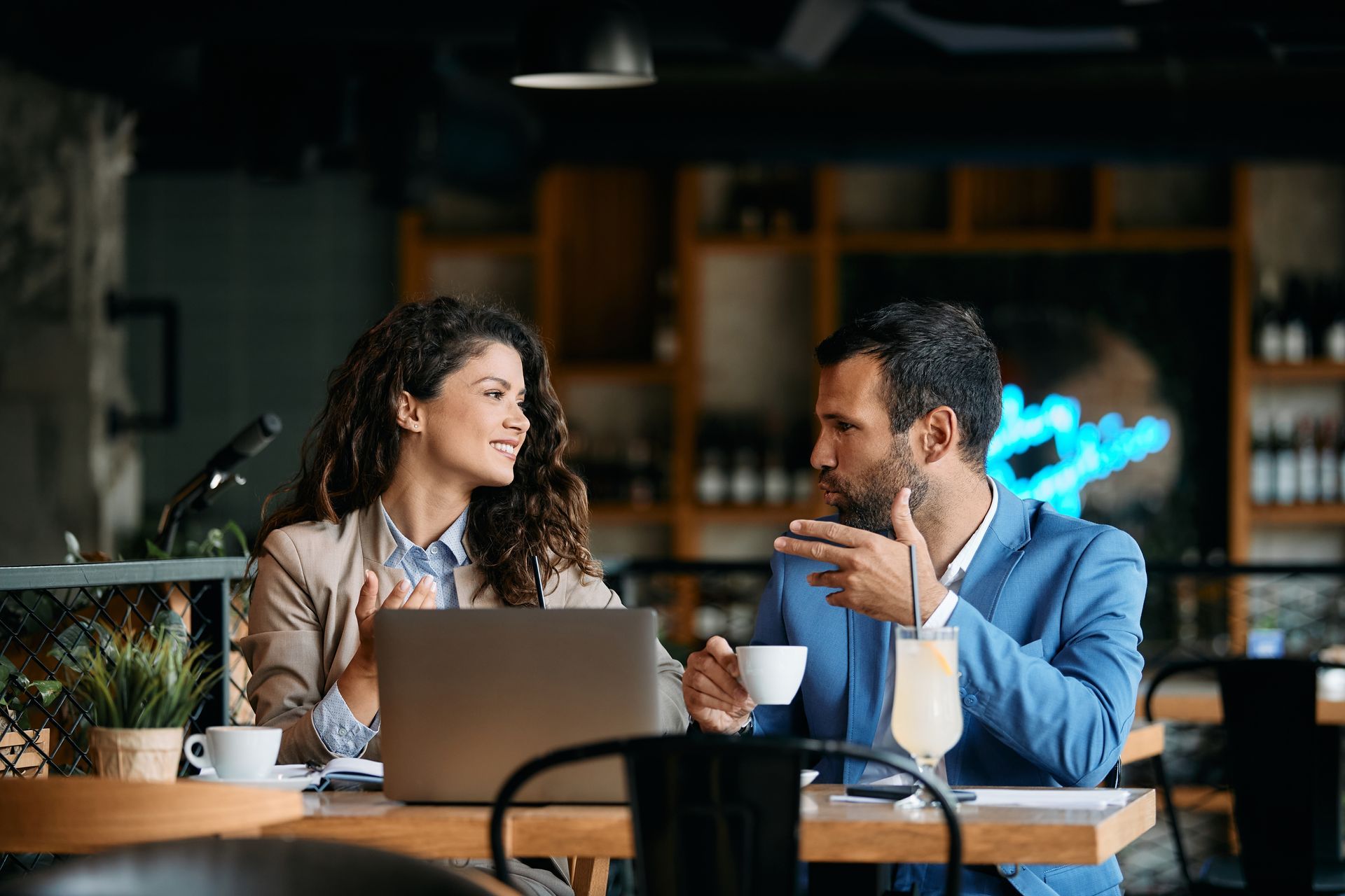 Two people talking at a café table with a laptop and coffee cups