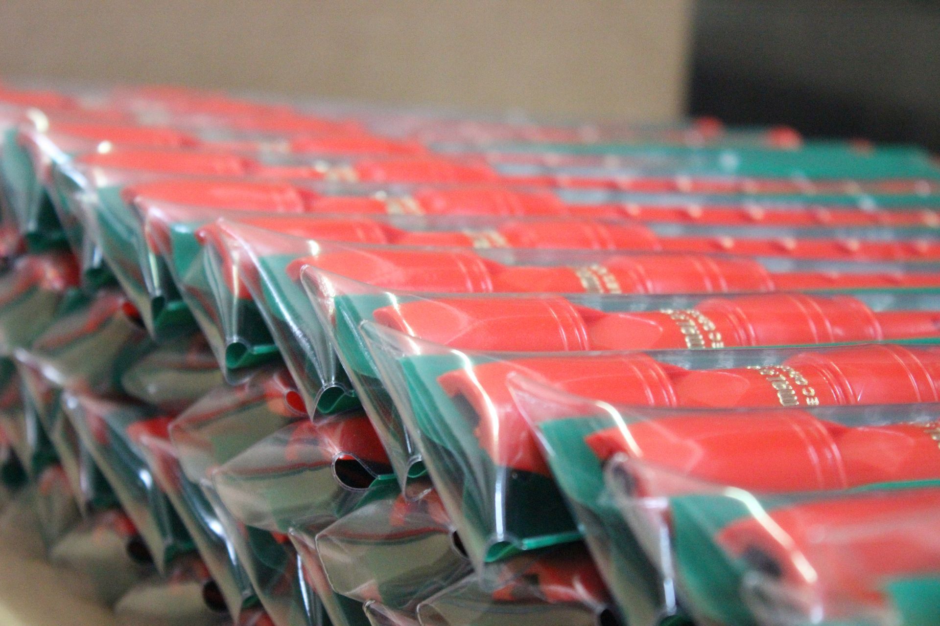 Pile di articoli confezionati in rosso e verde, avvolti in plastica trasparente, disposte in file su un tavolo.