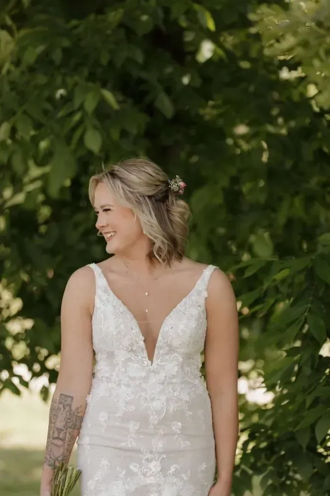 Woman in a white lace dress standing outdoors against a leafy green background