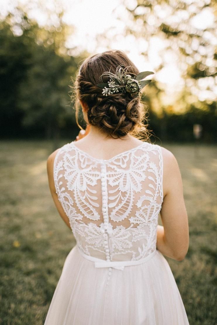 Back view of a woman in a white lace dress standing outdoors in a sunlit field