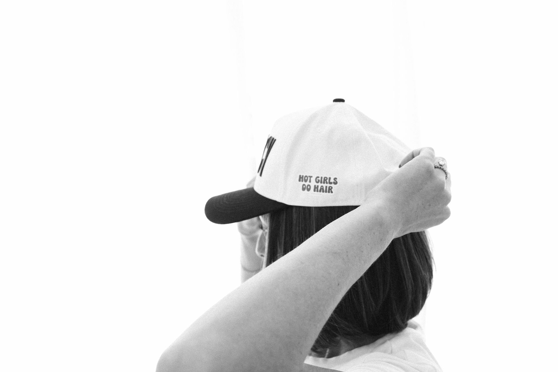 Person adjusting a white cap against a bright background