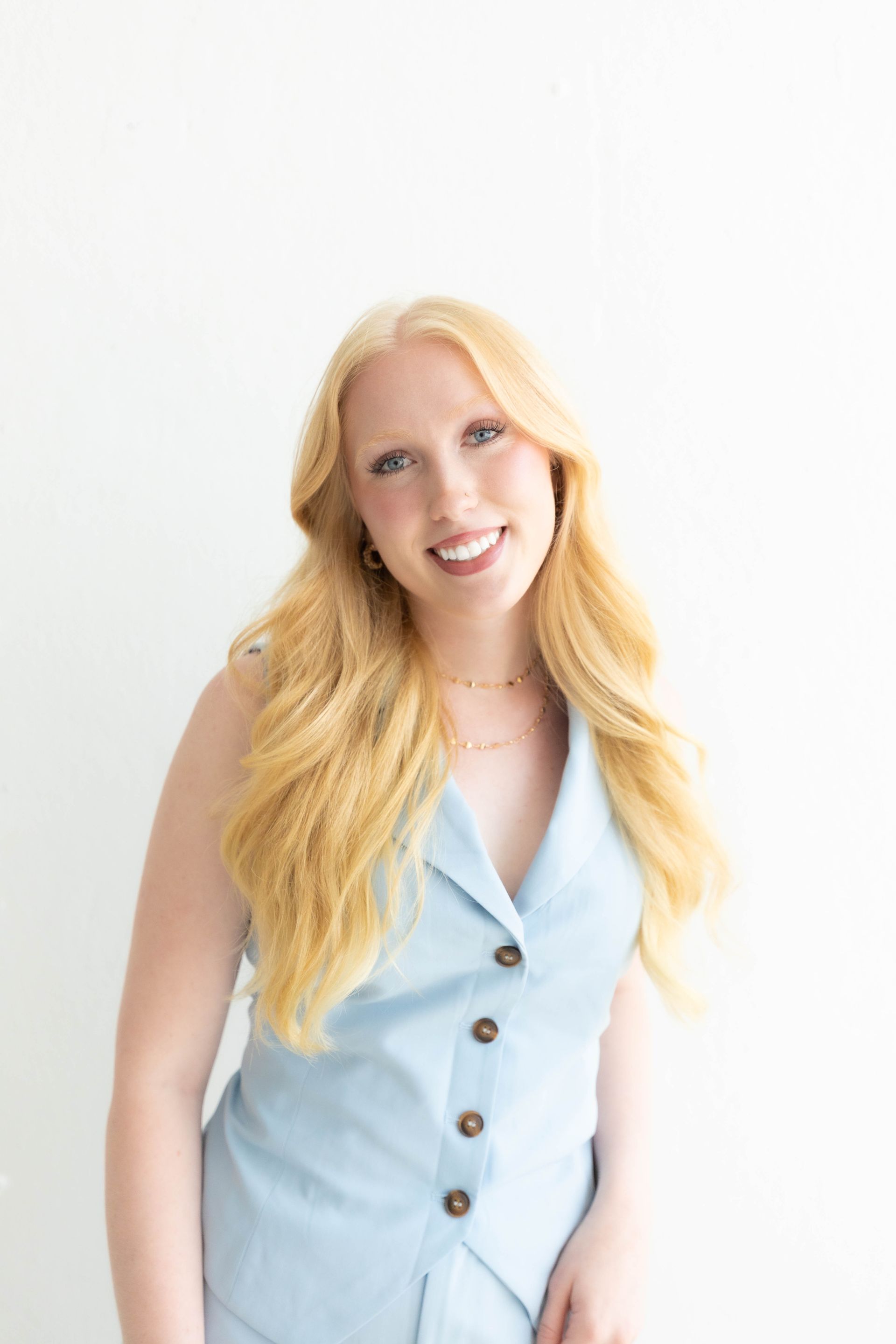 Smiling woman in a light blue sleeveless dress against a white background