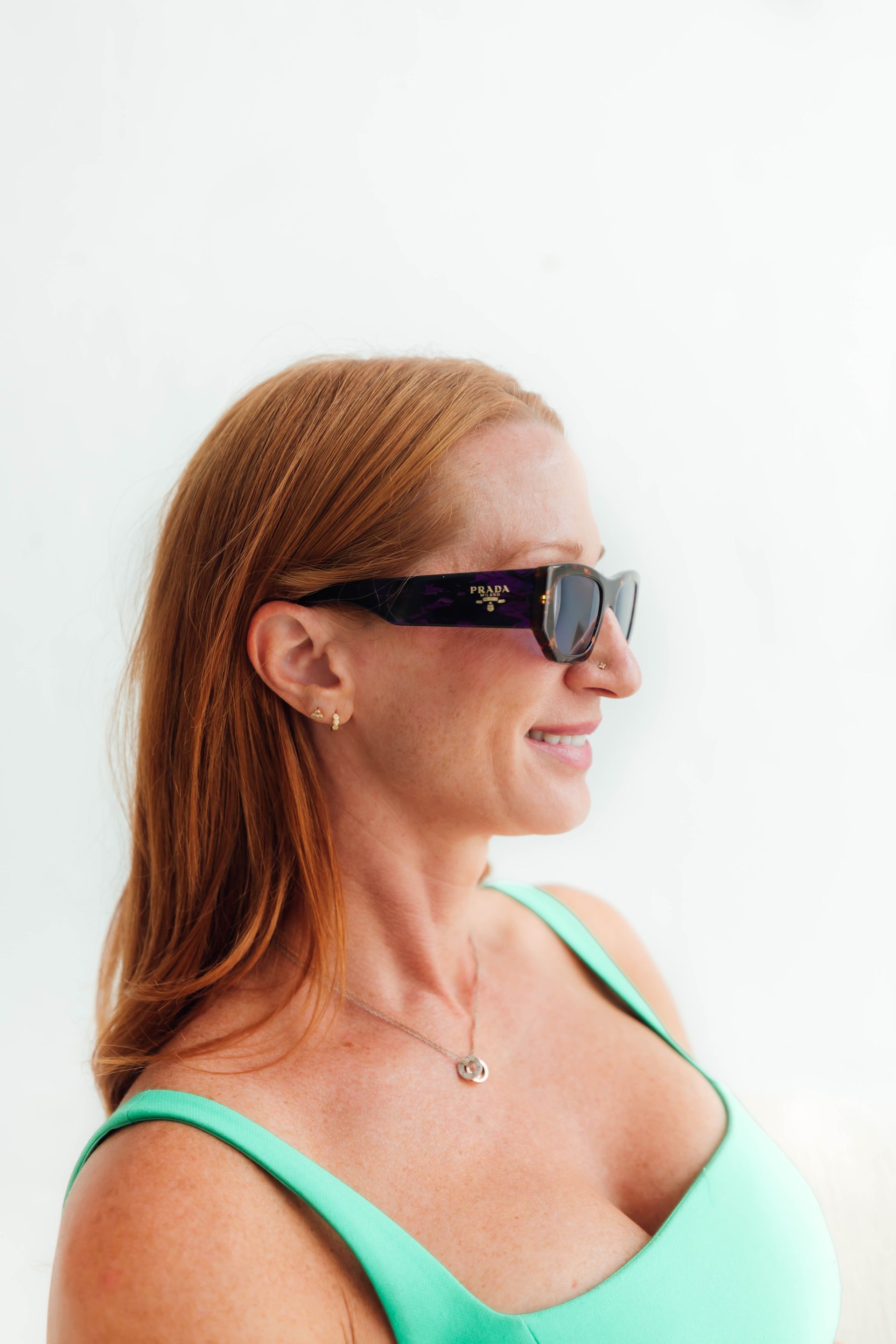 Woman in black sunglasses and a mint-green top, shown in profile against a white background.