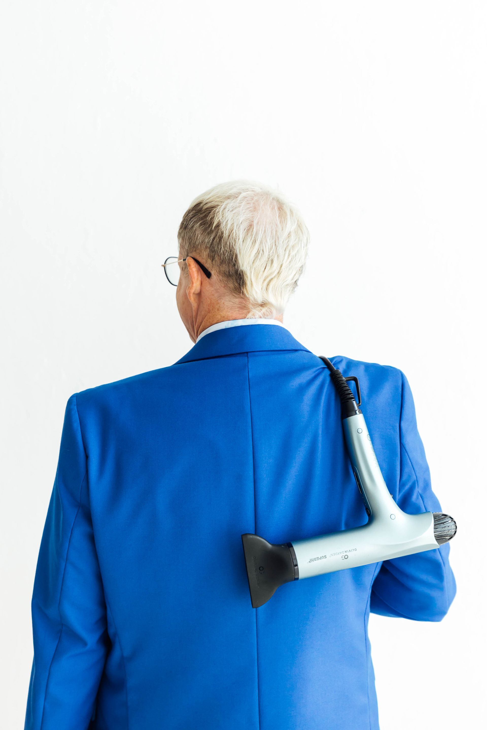 Person in a blue jacket with a crutch slung over their back, seen from behind.
