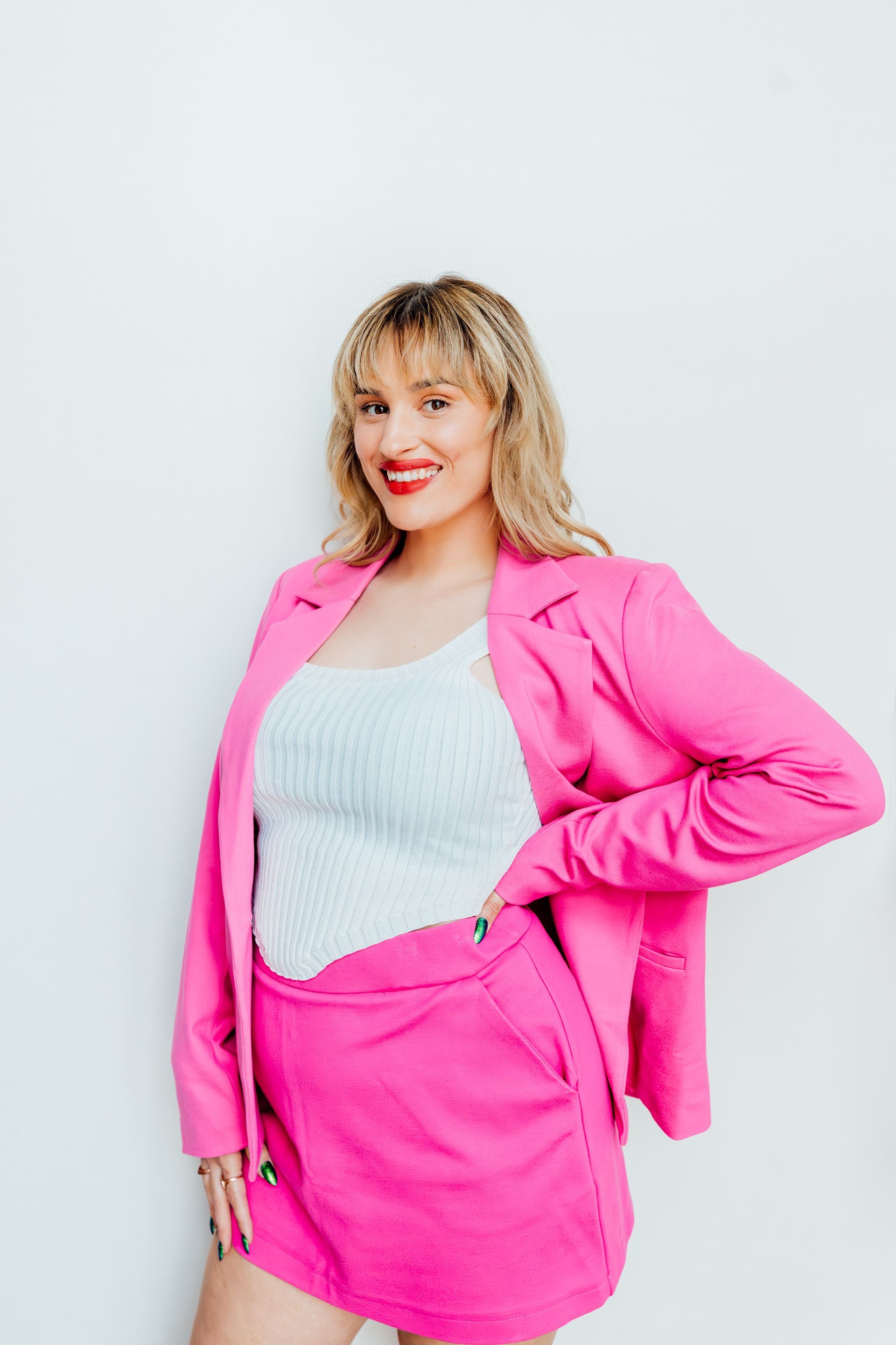 Woman in bright pink blazer and skirt over a white top, smiling against a plain light background