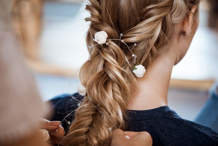Braided hair being styled with white flowers by a blurred person in the background