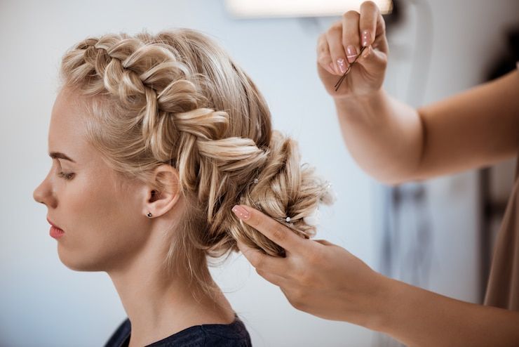 Braiding blonde hair in a salon, with hands weaving a side braid.