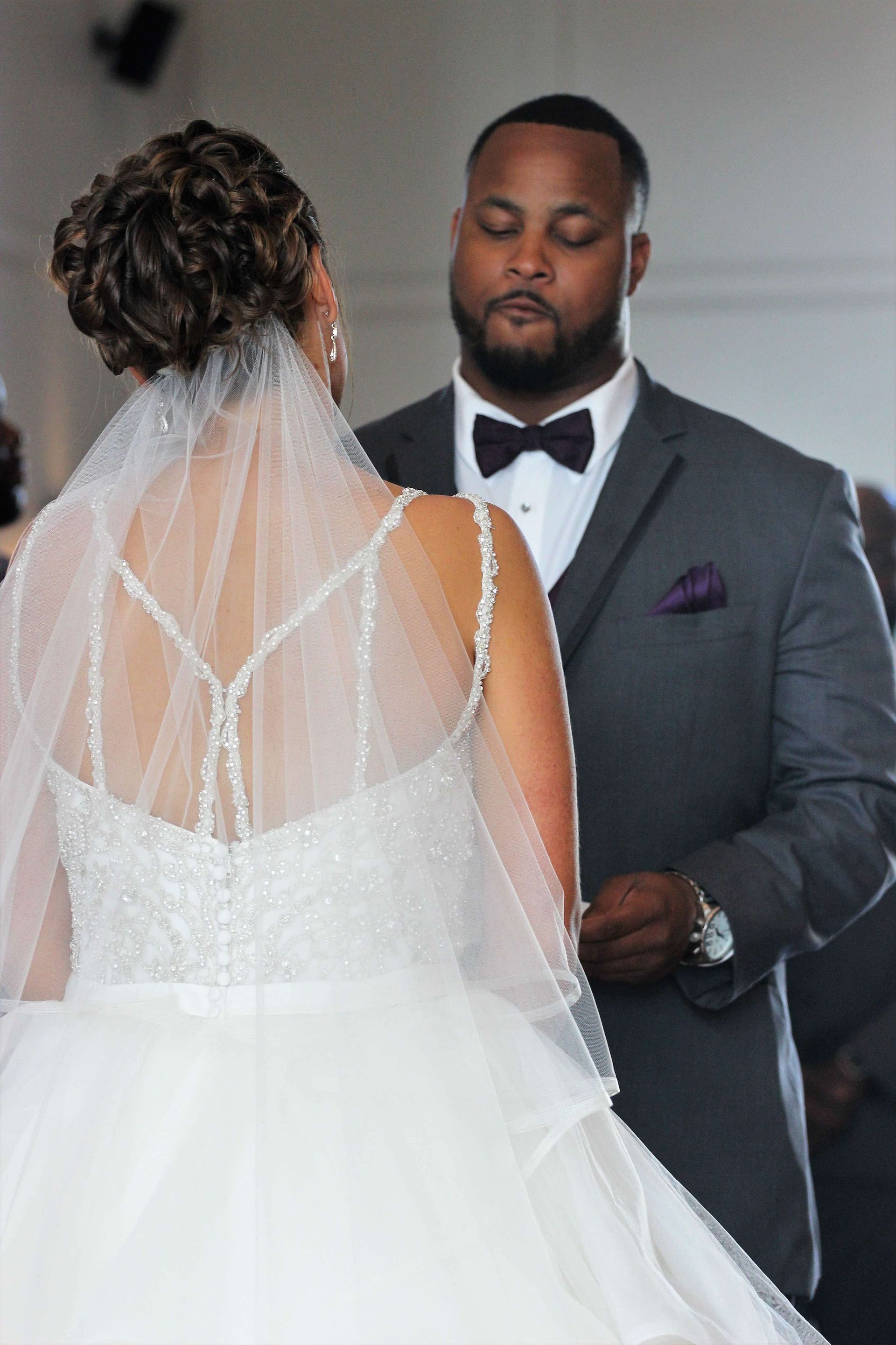 Bride and groom exchanging vows at a wedding ceremony, with the groom in a gray suit and the bride in a white gown and veil