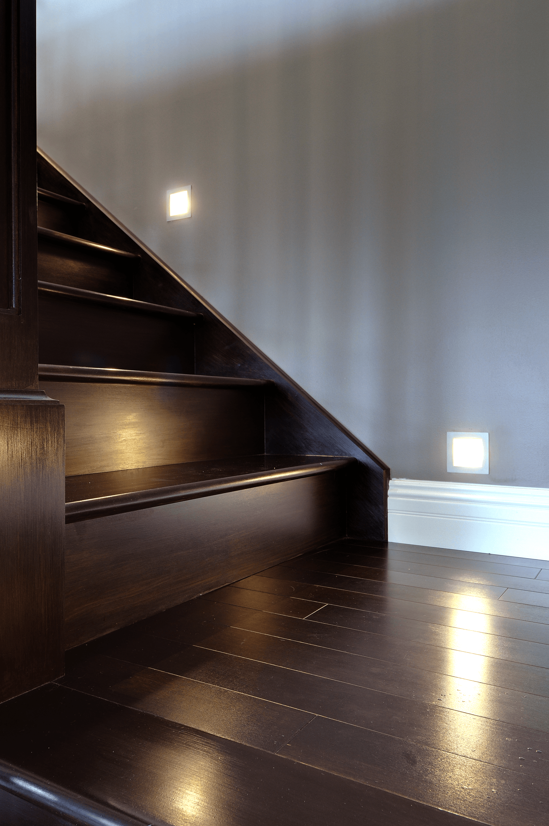 A close up of a wooden staircase with a light on the bottom step.