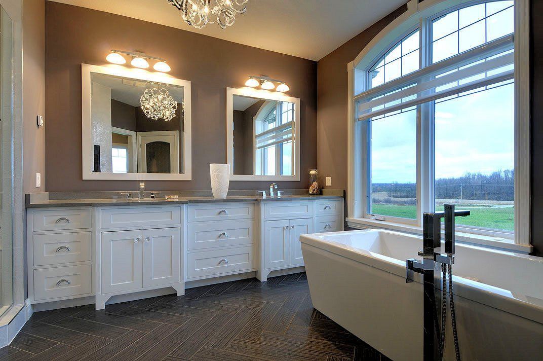 A bathroom with a tub , sinks , mirrors and a large window.