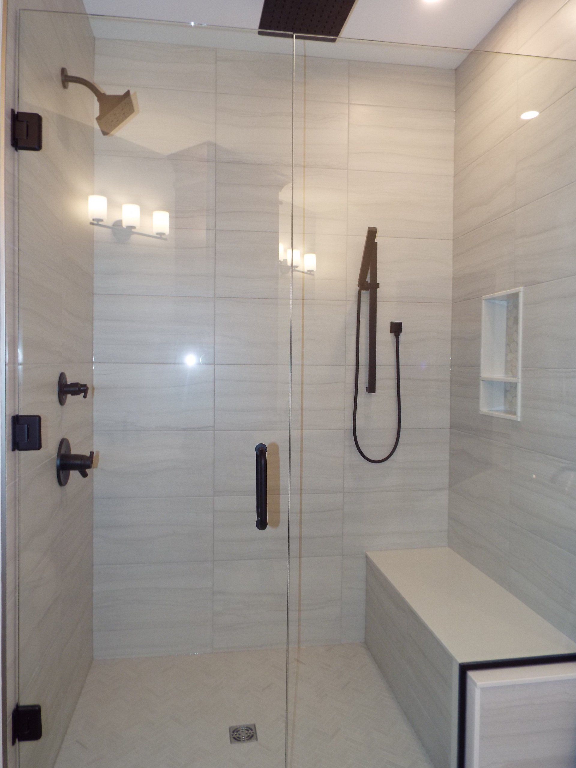 A walk in shower with a glass door and a bench