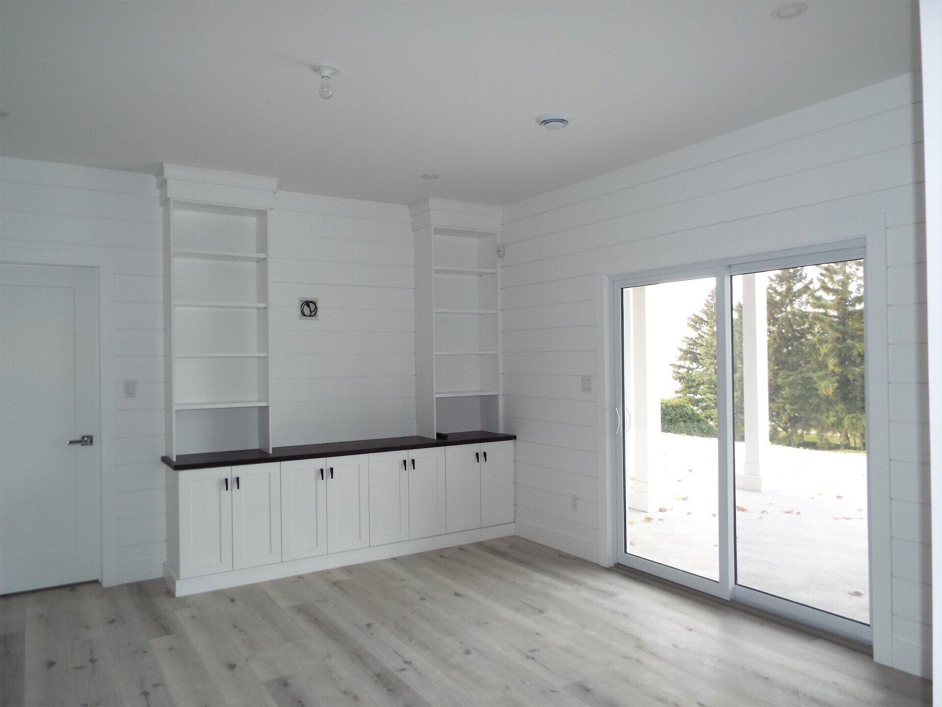 An empty living room with white cabinets and sliding glass doors.