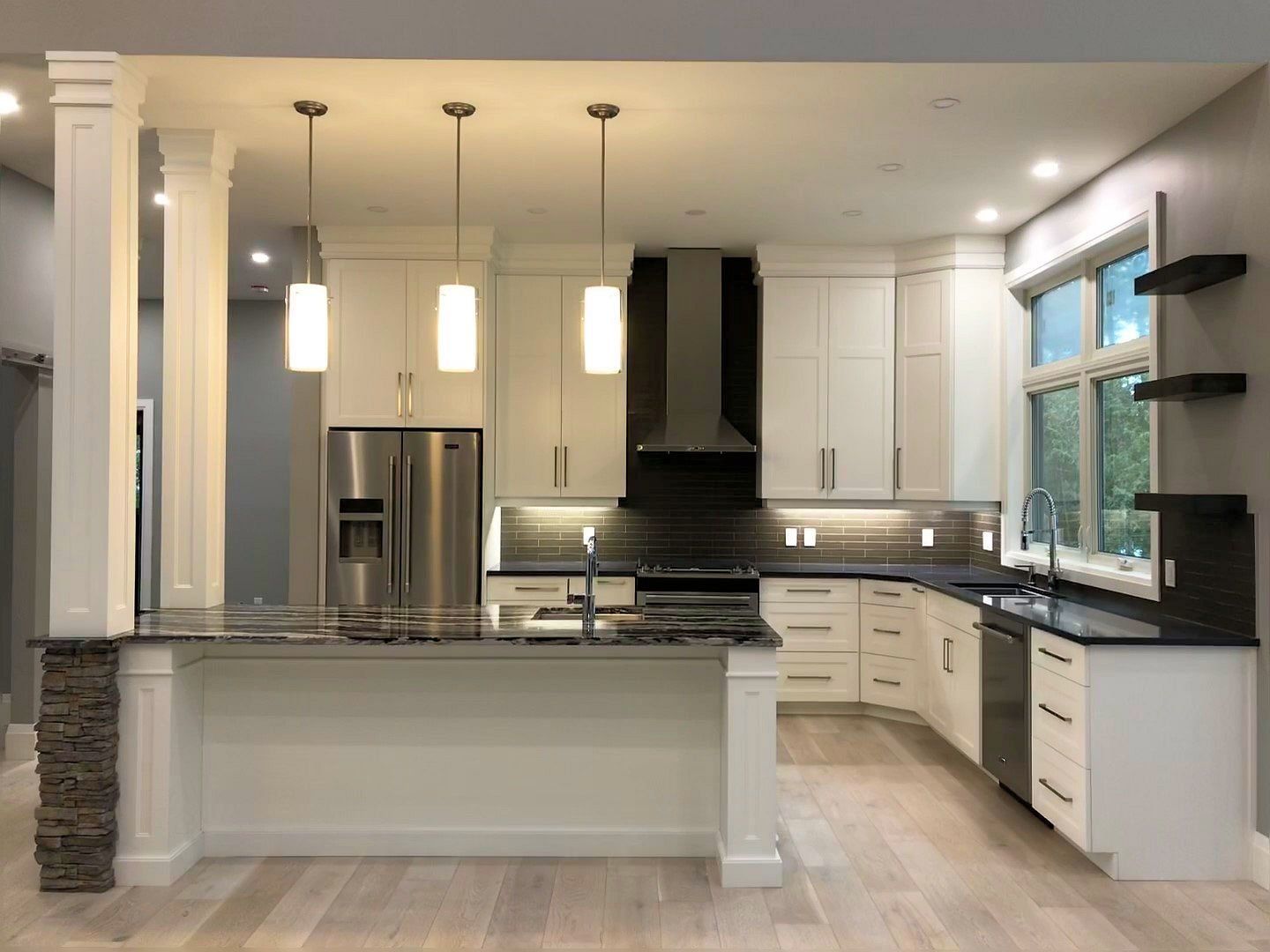 A kitchen with white cabinets , black counter tops , stainless steel appliances and a large island.