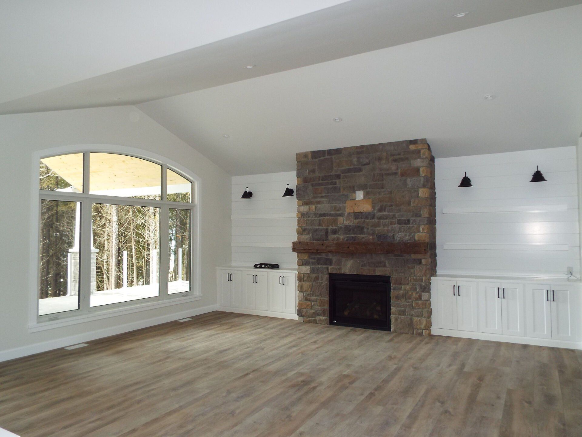 An empty living room with a stone fireplace and large windows.