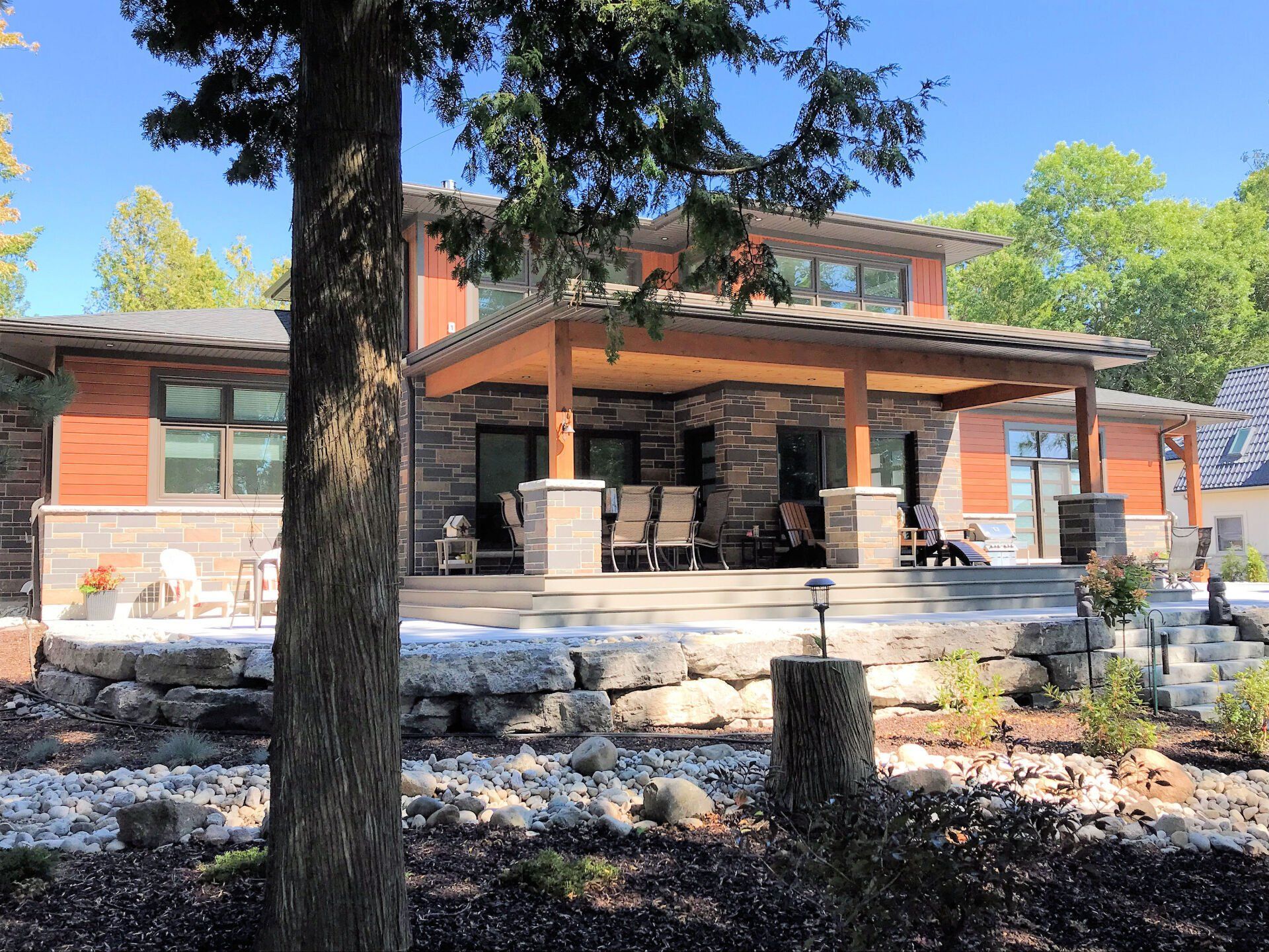 A modern two-story home with wood siding and stone accents featuring a large covered patio and a tiered rock terrace.