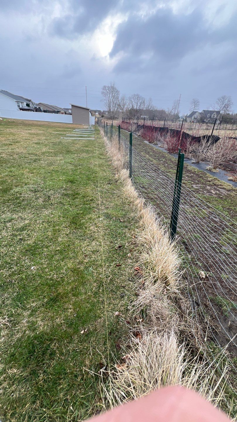Fence along grassy field under cloudy sky, with houses and trees in the distance.