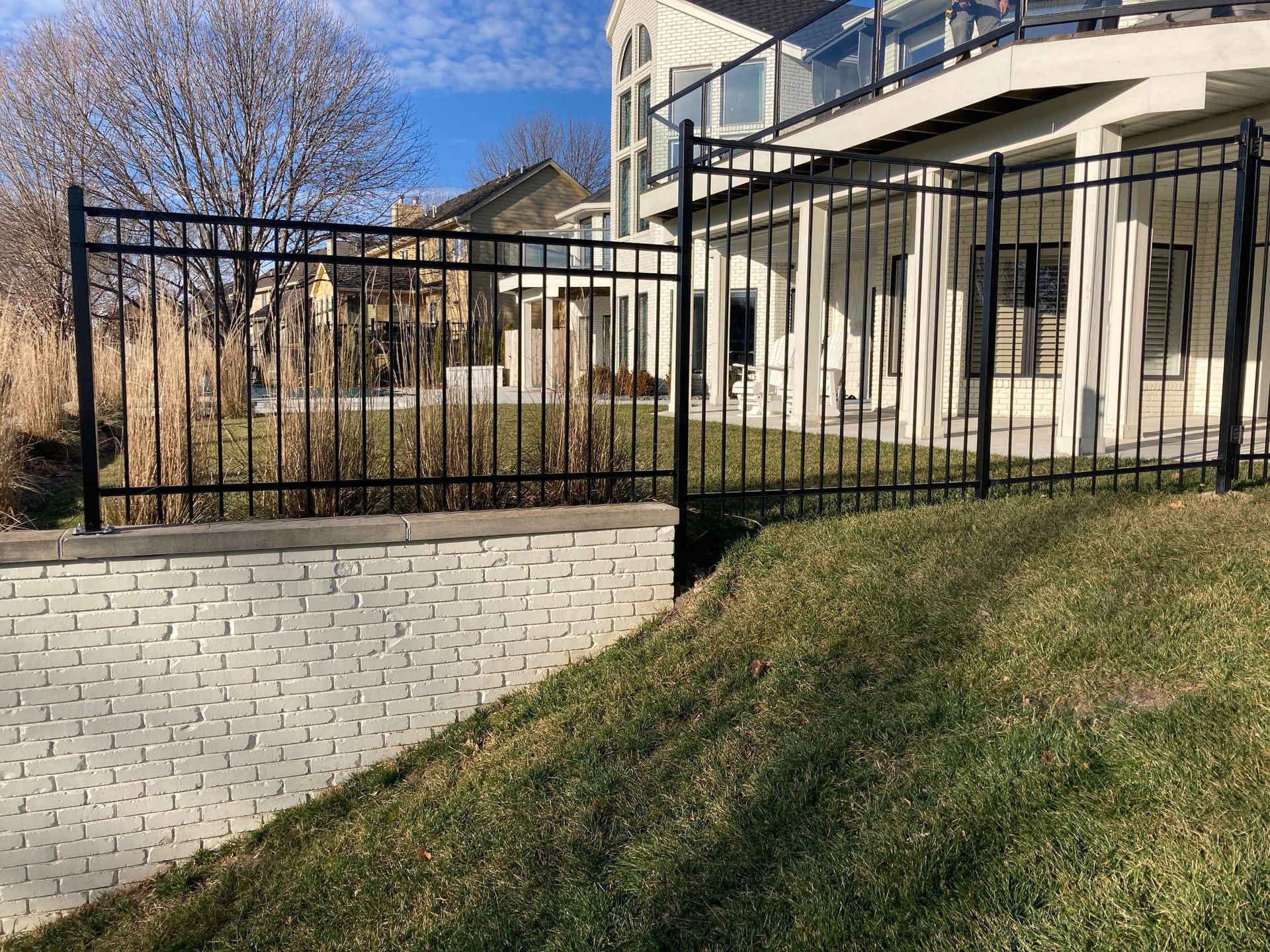 White house with black fence beside a grassy slope under a blue sky