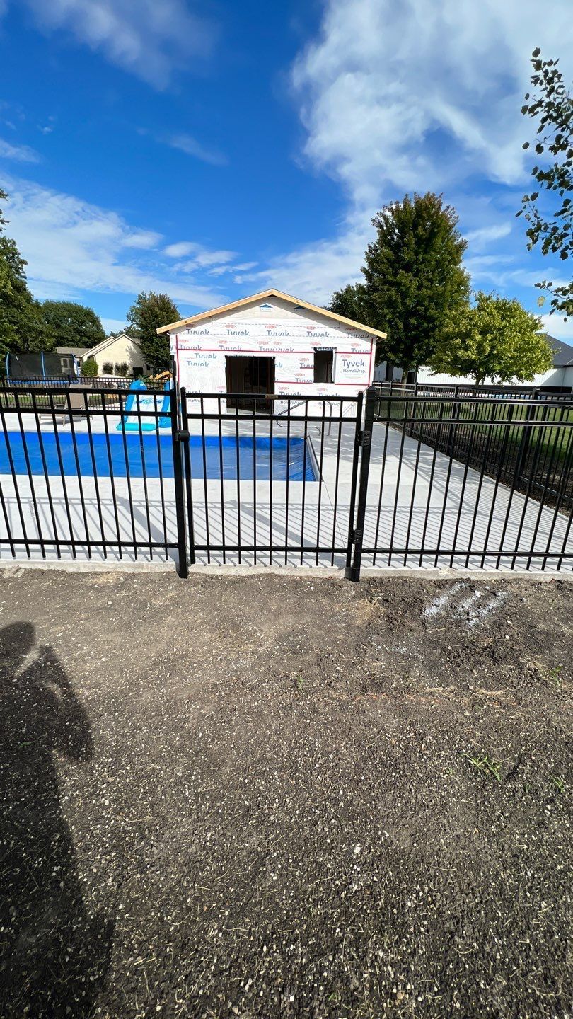 Backyard with a blue pool, white shed, and black gate under a bright sky.