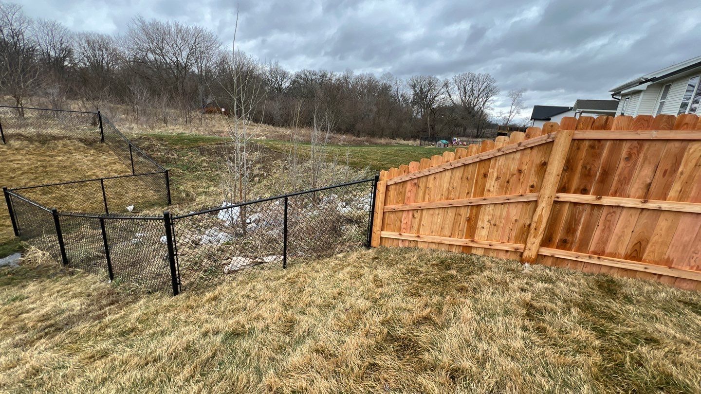 Backyard hillside with chain-link and wooden fences under a cloudy sky