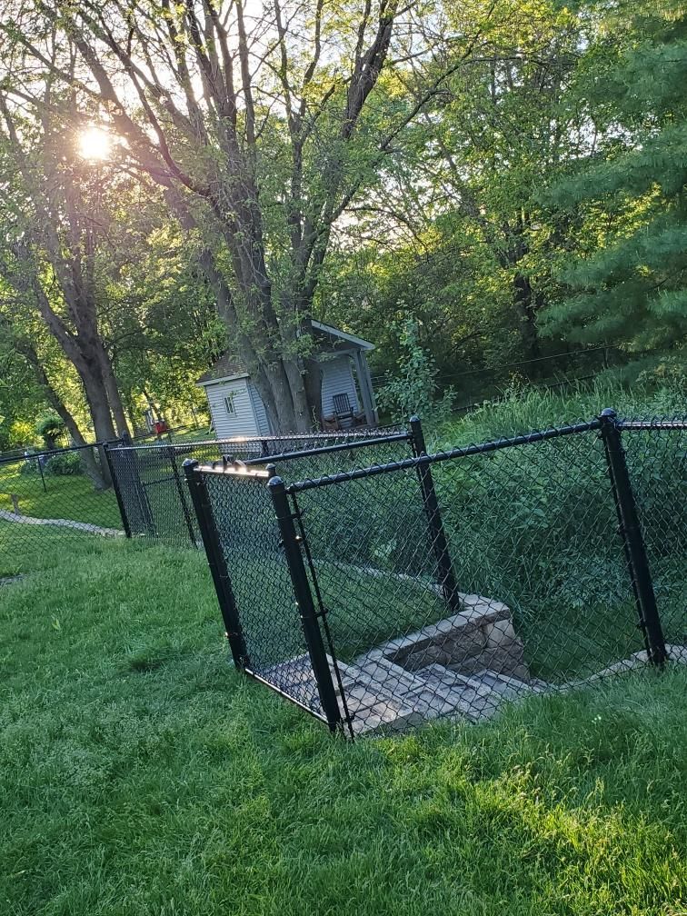Small fenced utility structure beside a grassy path in a wooded park at sunset