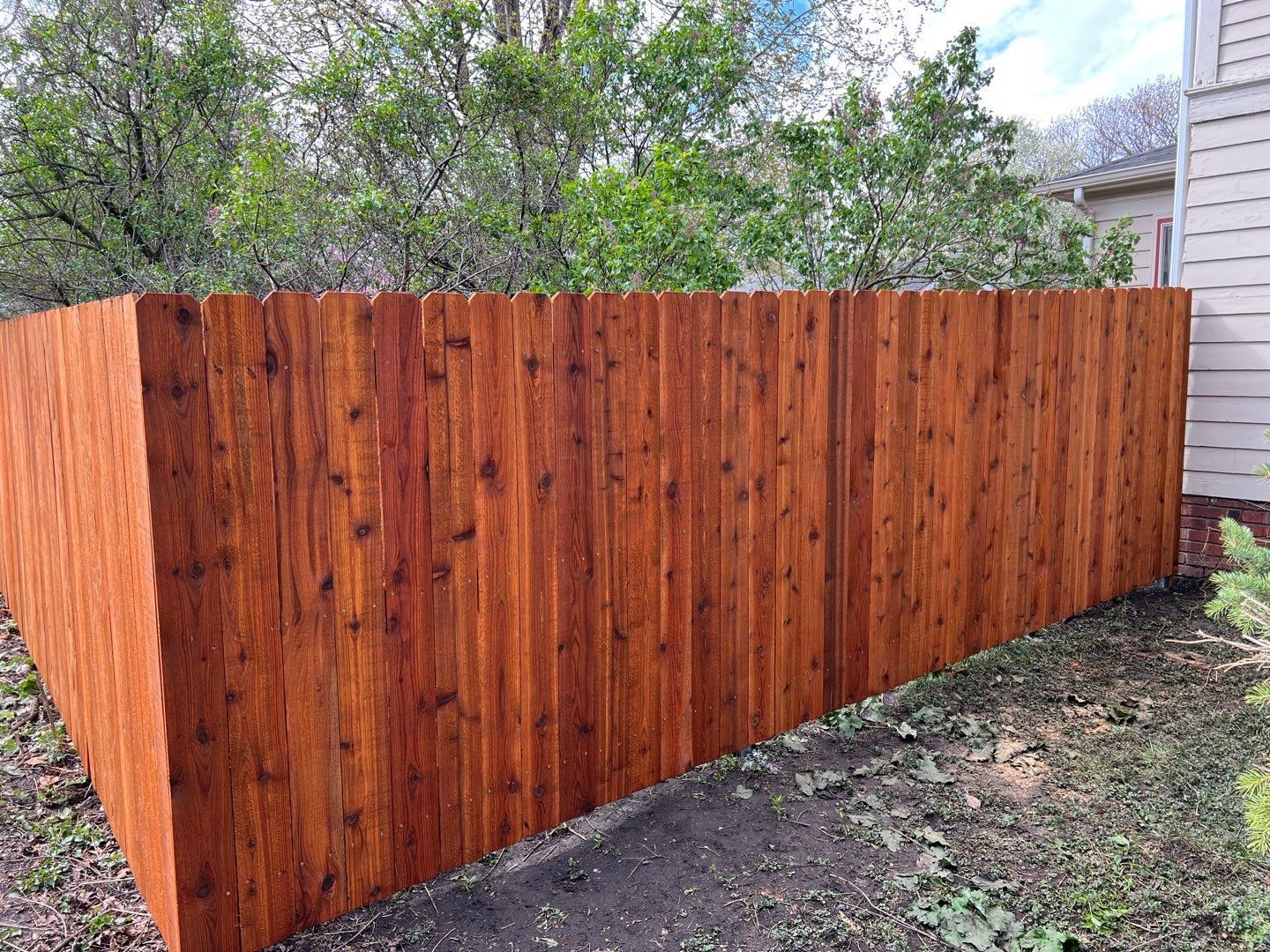 Stained wooden privacy fence with lattice top beside a house and gravel yard