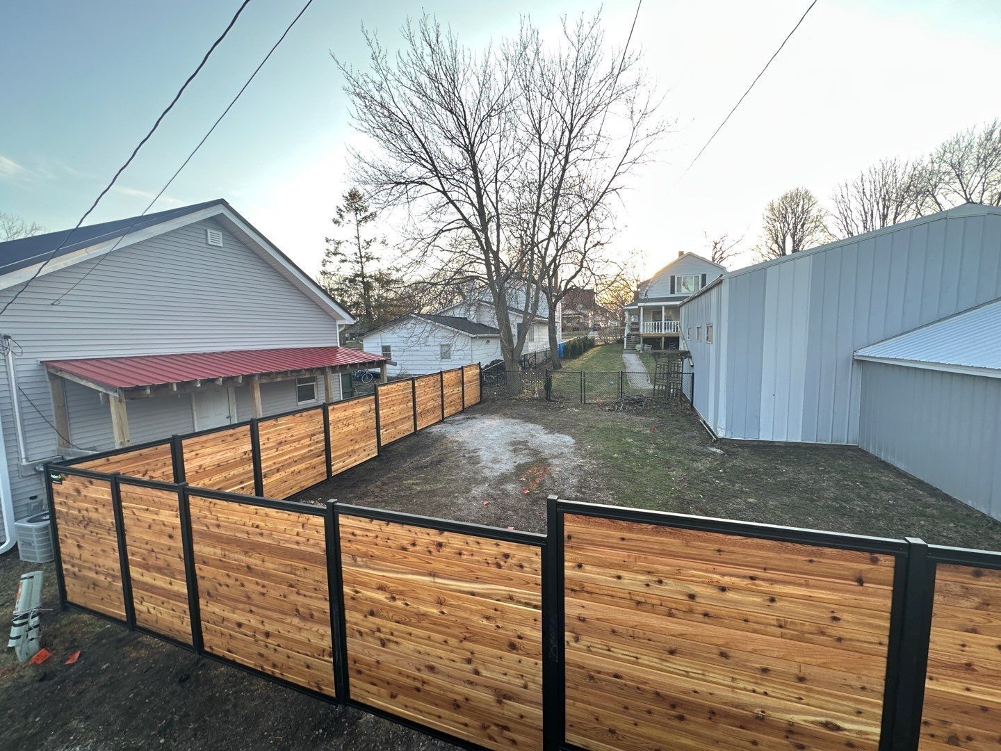 Backyard with wooden privacy fence, bare trees, and two houses under a clear sky
