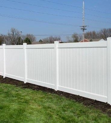 White vinyl privacy fence along a grassy yard under a clear blue sky