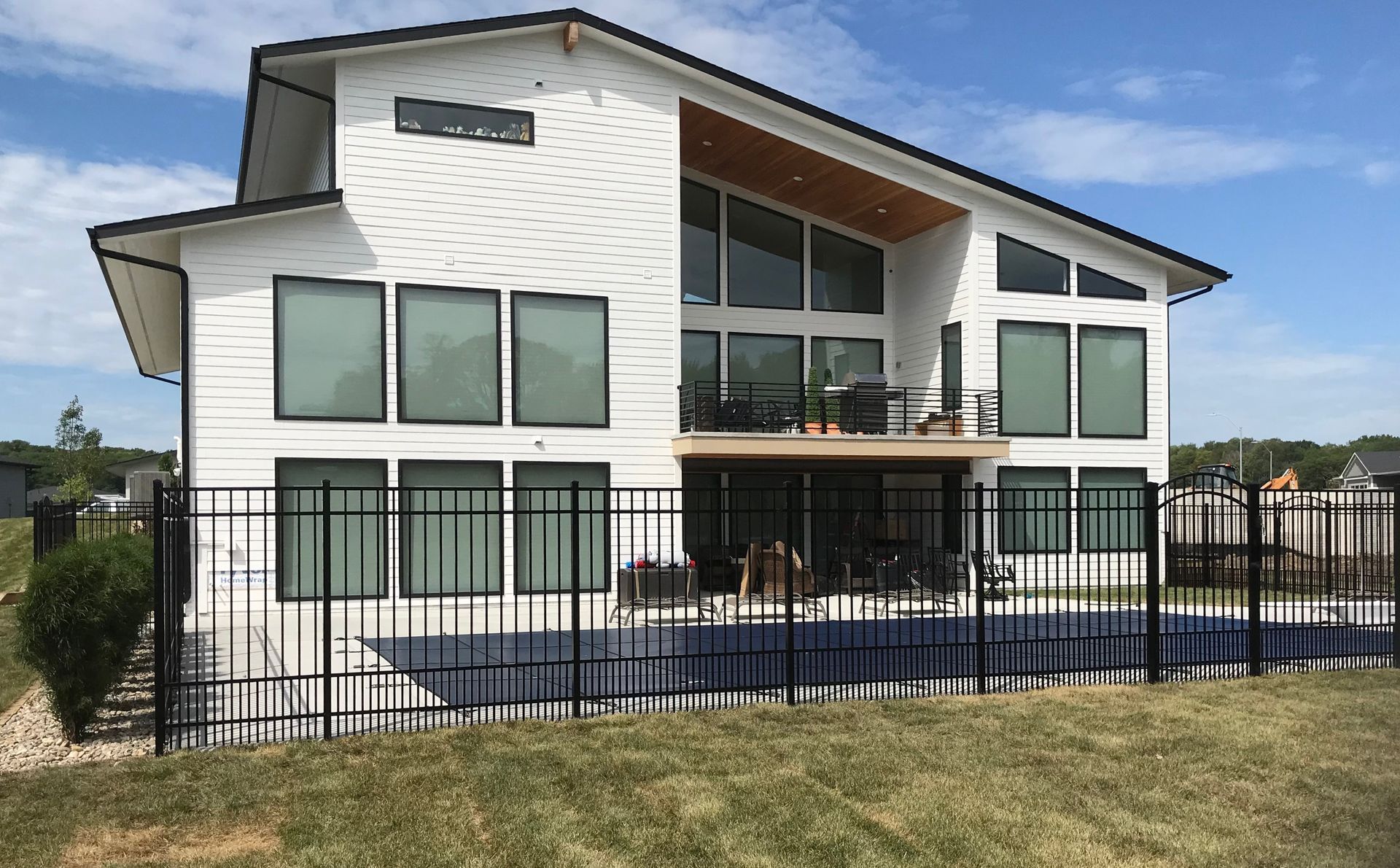 Modern white two-story house with large windows, a balcony, and a black metal fence in front
