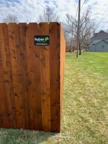 Wooden privacy fence with a small Huber sign beside a grassy yard and bare trees