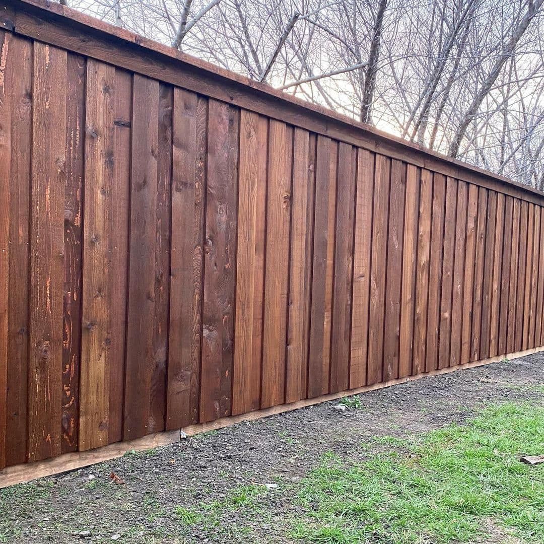 Wooden privacy fence along a sloped yard with bare trees and patchy grass