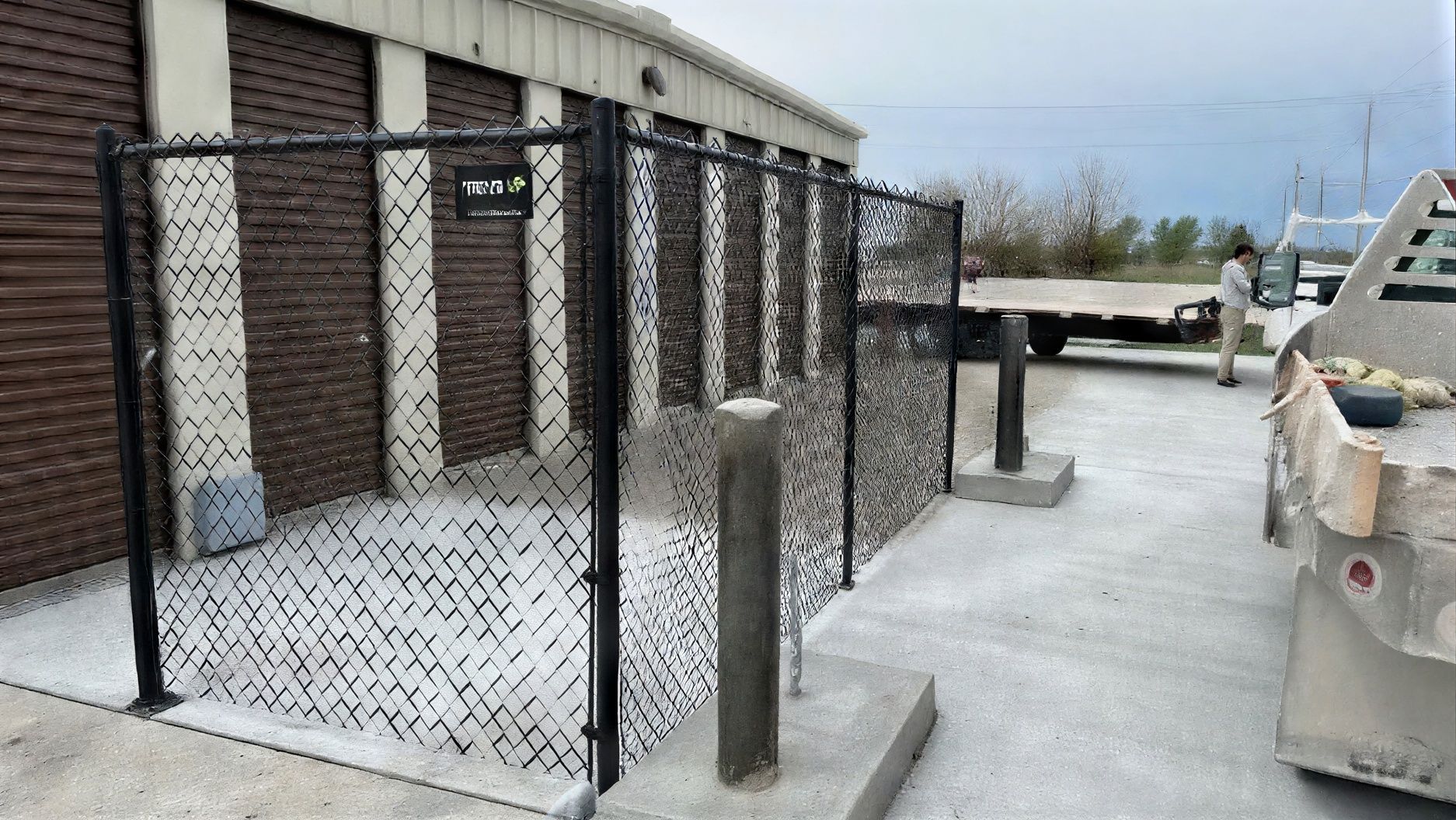 Freshly installed black chain link commercial fence with concrete footings at a business facility