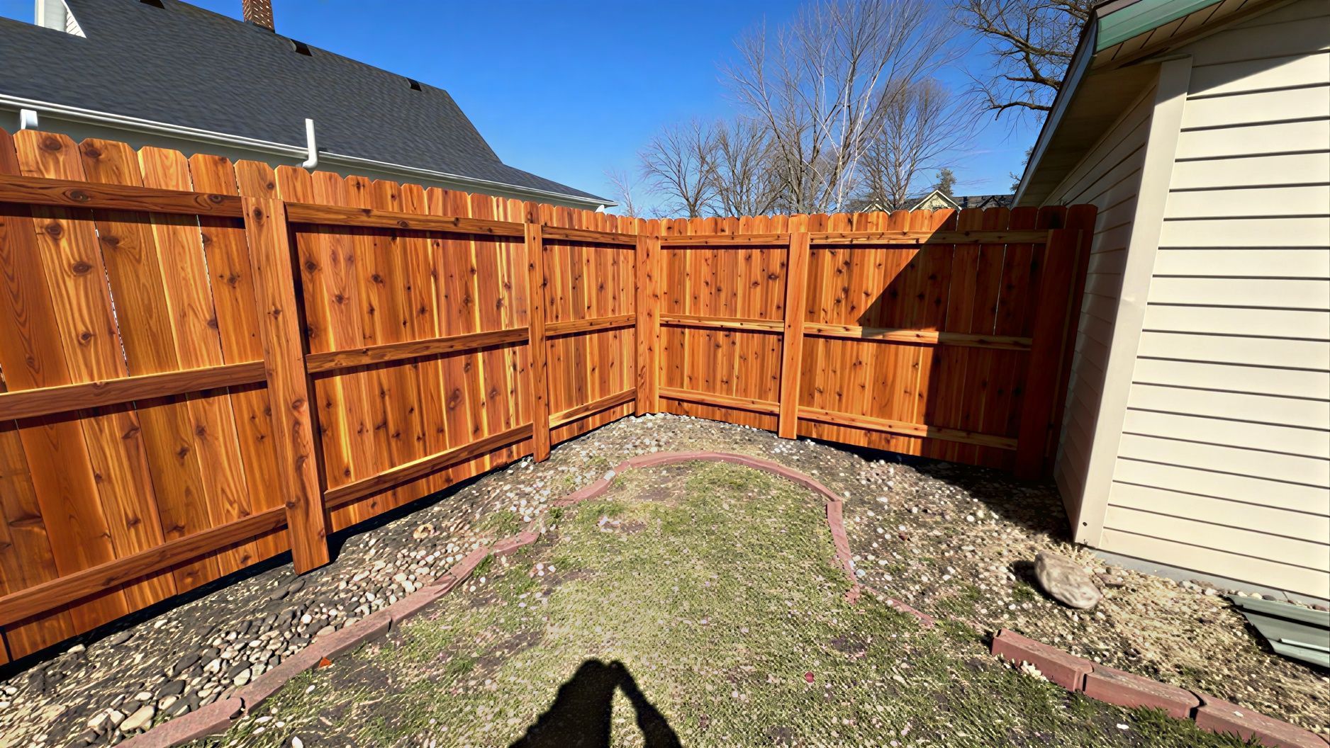 A new wooden privacy fence enclosing a backyard corner with a gravel border and grass lawn