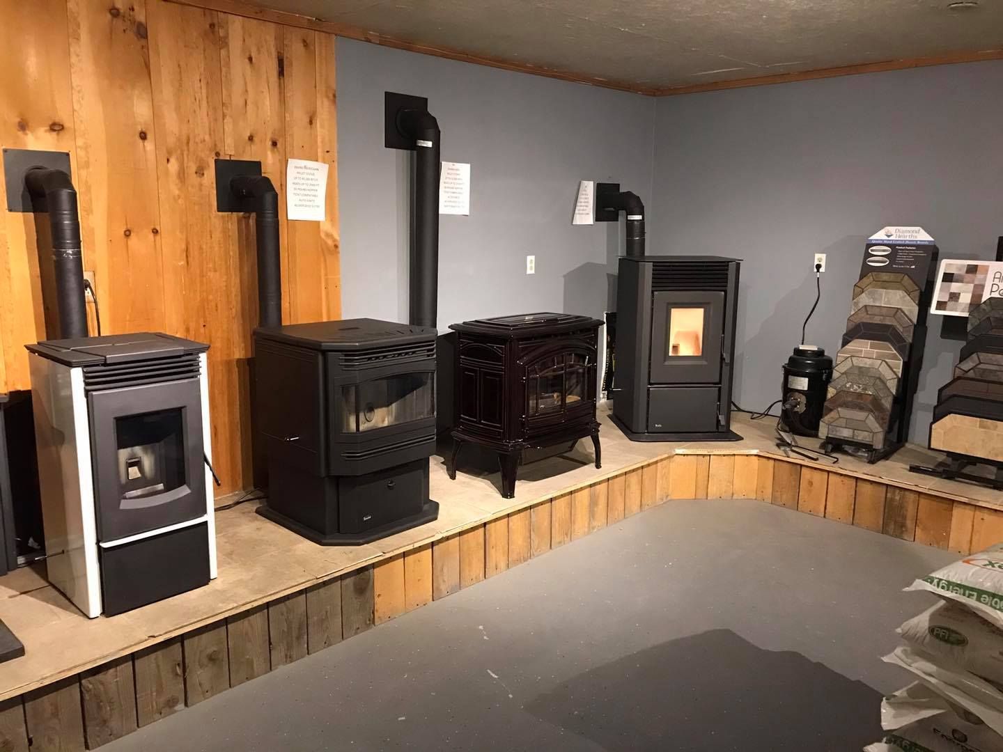 Wood-burning stoves in a showroom. Various models, black and dark colors, set against wood and gray walls.