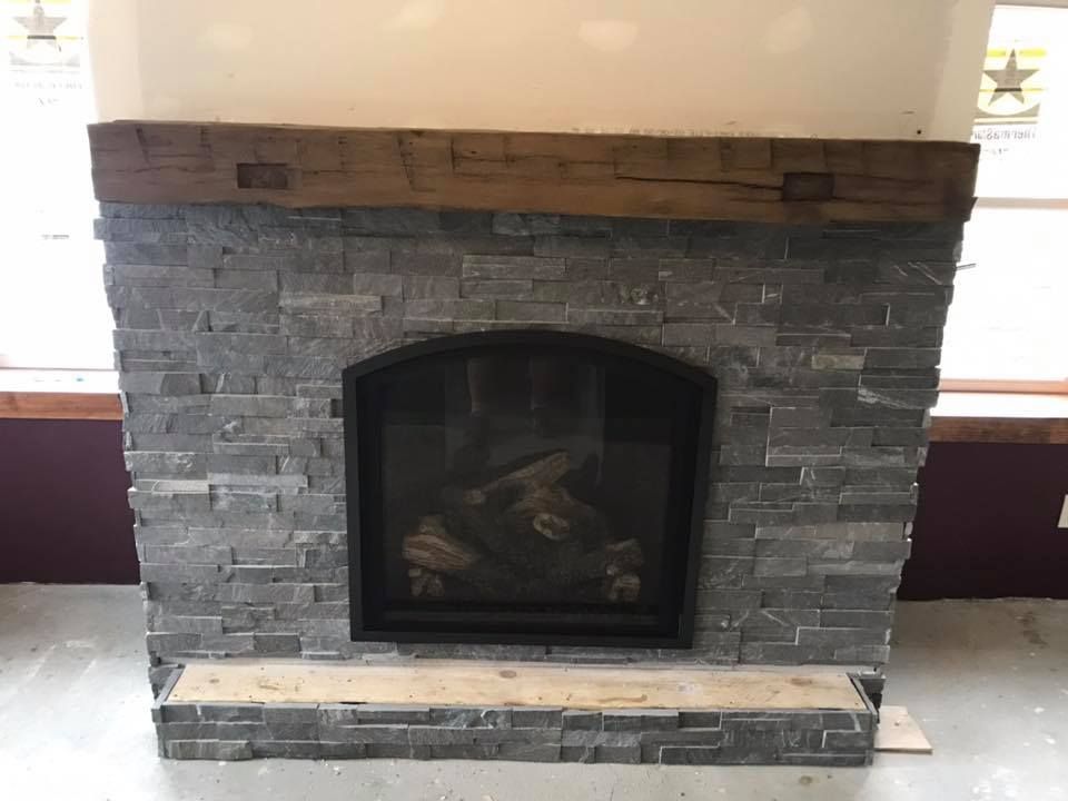 Fireplace with gray stone facing and a wooden mantel.