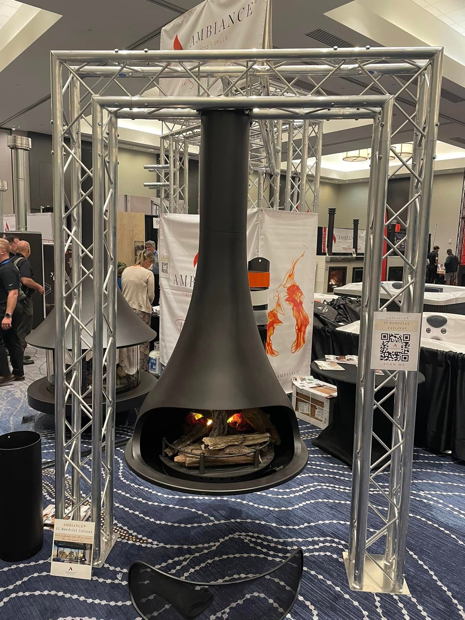A black fireplace with a long chimney is displayed in a metal frame at an exhibition.