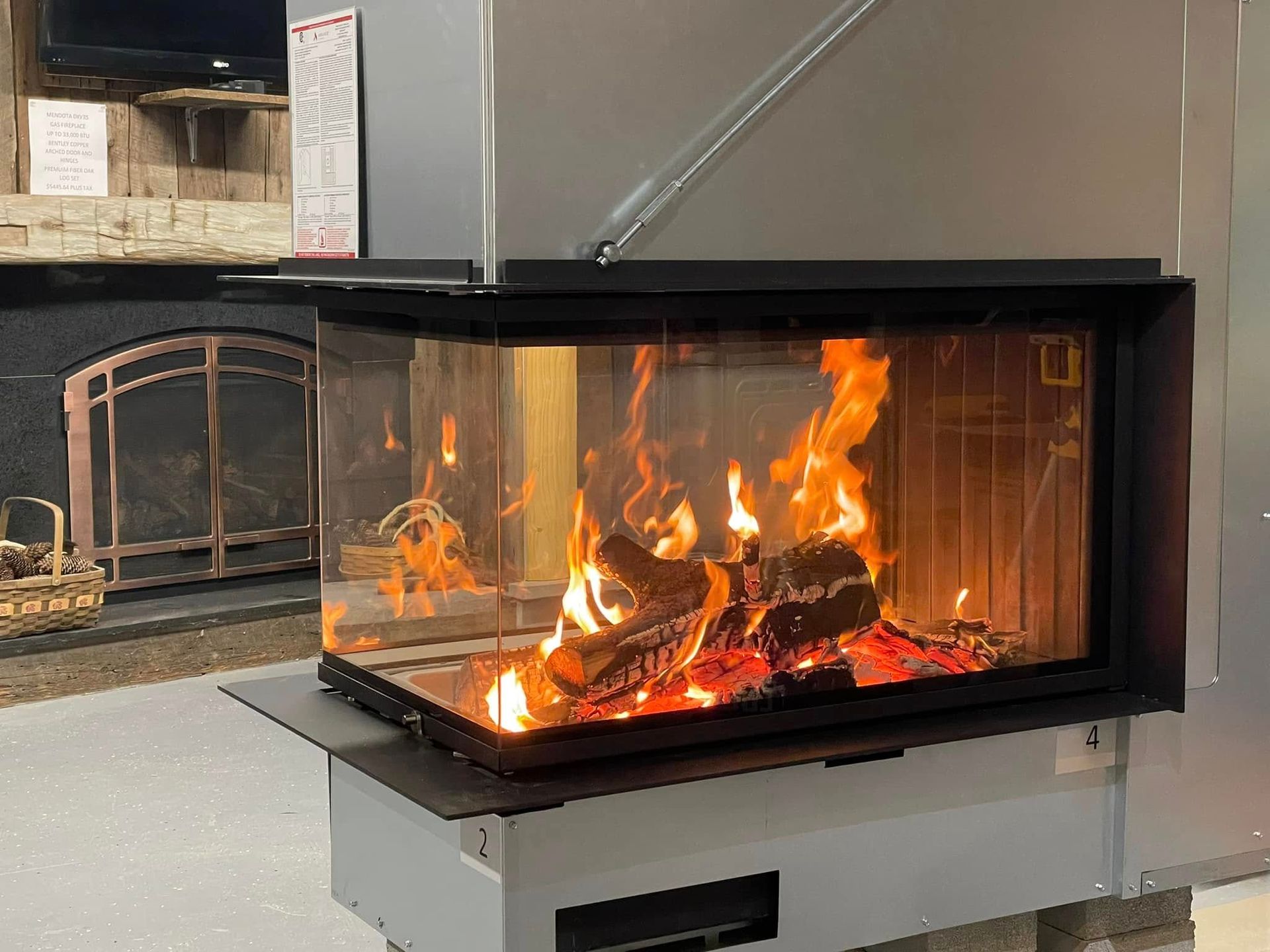 Fireplace with three glass sides filled with burning logs, inside a showroom.