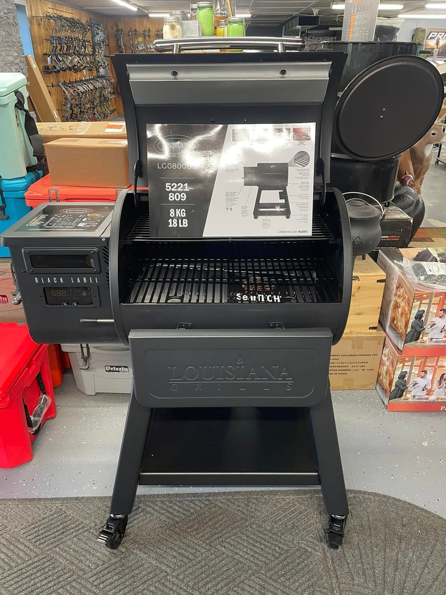 Black pellet grill with open lid, display inside a store.