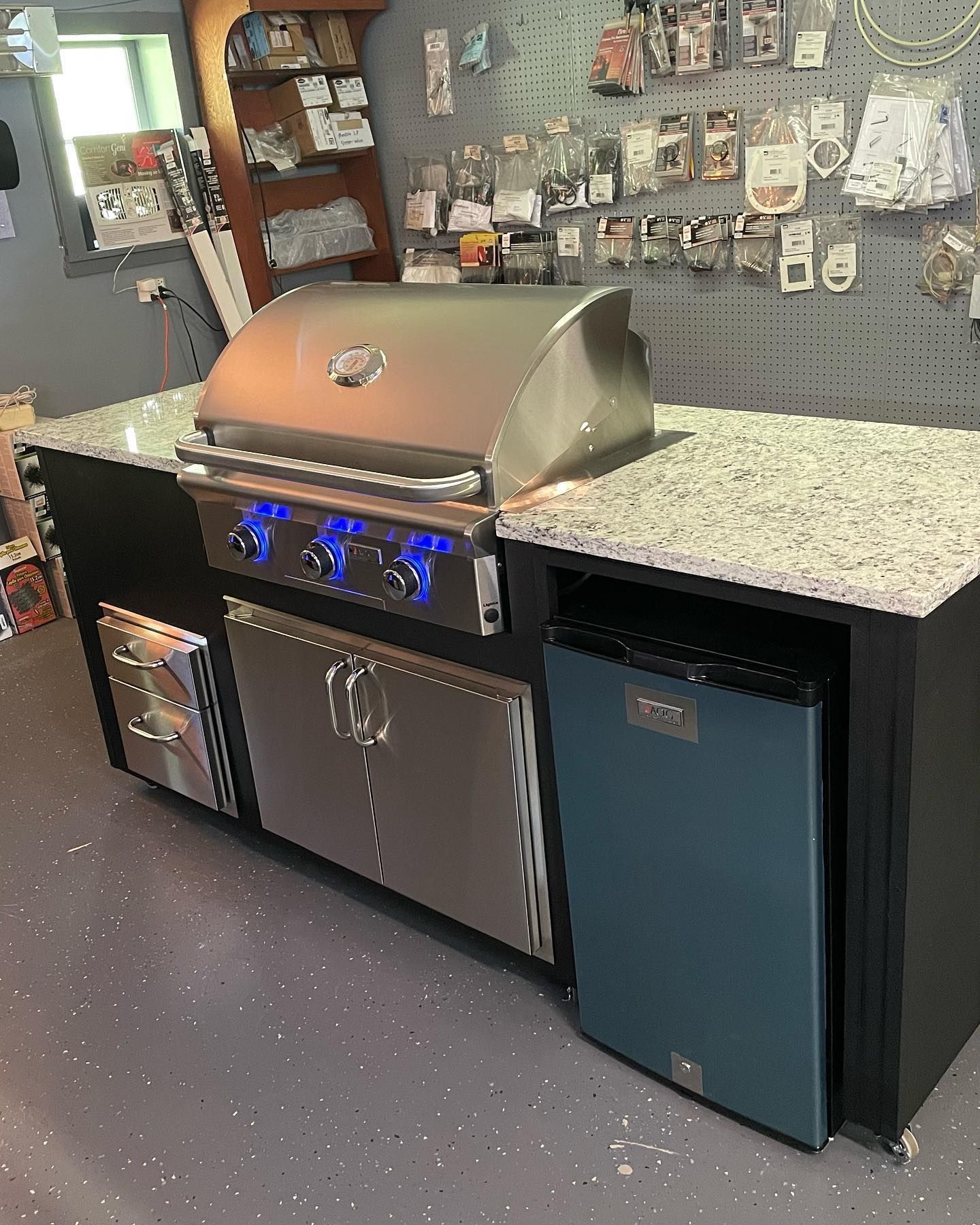 Outdoor kitchen island with stainless steel grill, refrigerator, and granite countertop.