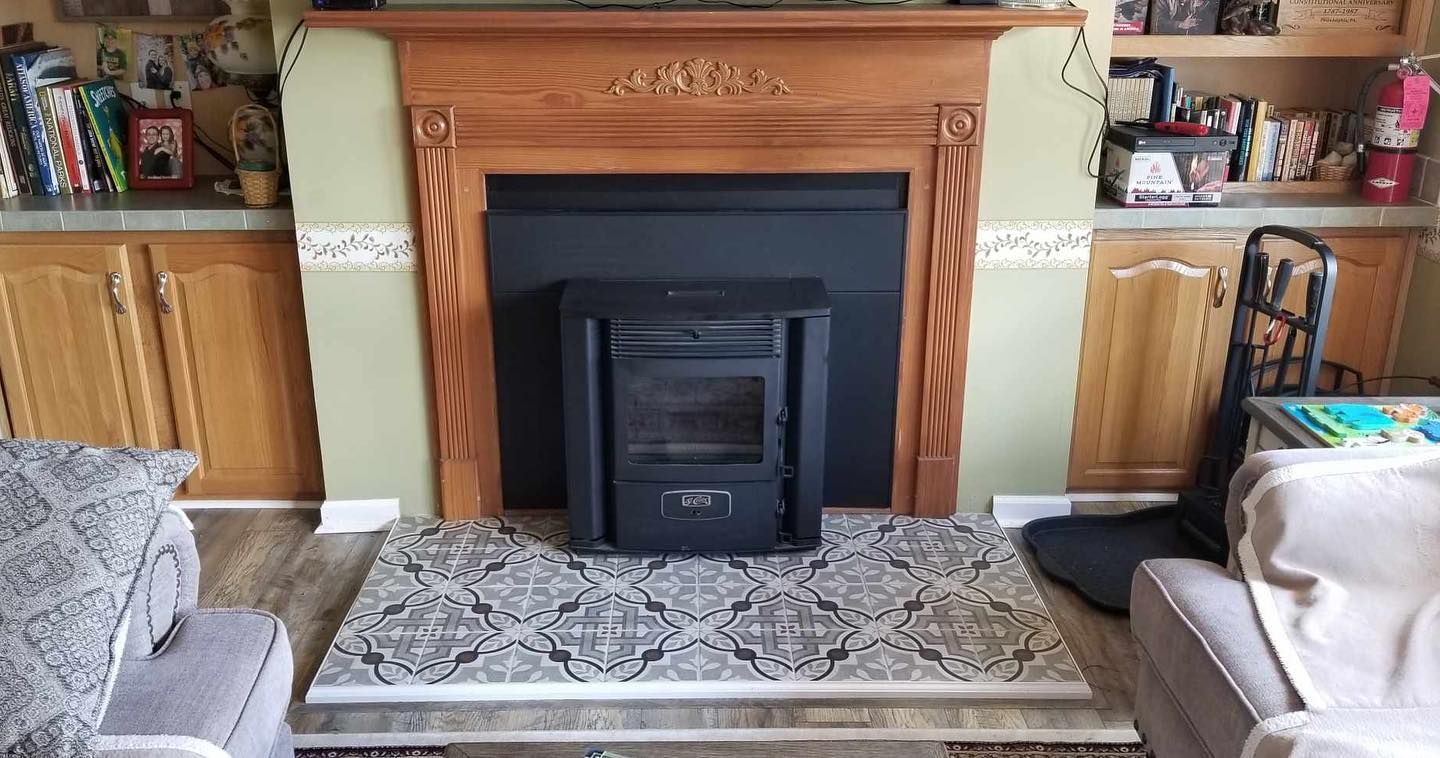 Black fireplace insert in front of a wooden mantle with a patterned rug.