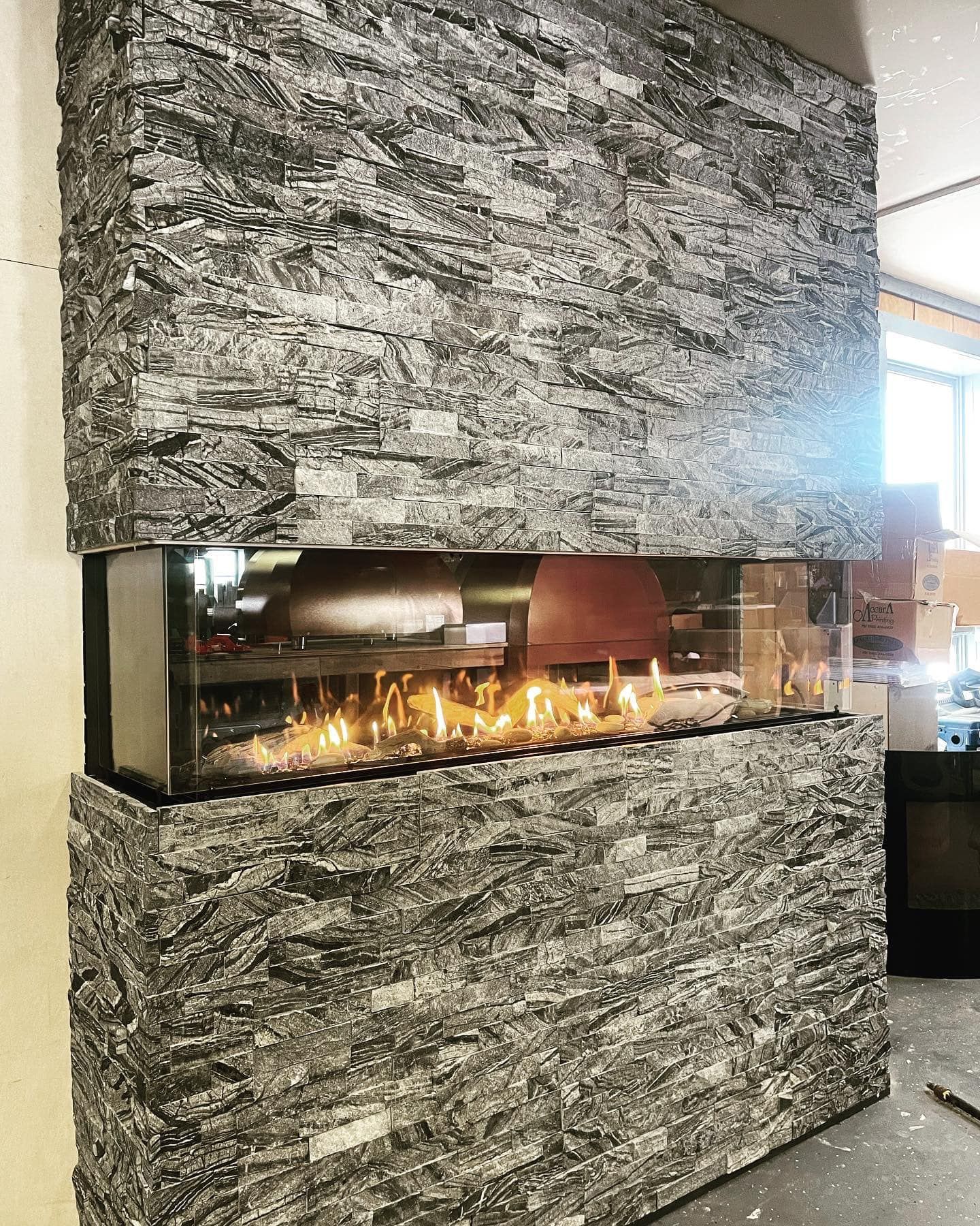 Modern fireplace encased in textured gray stone, flames visible through glass.