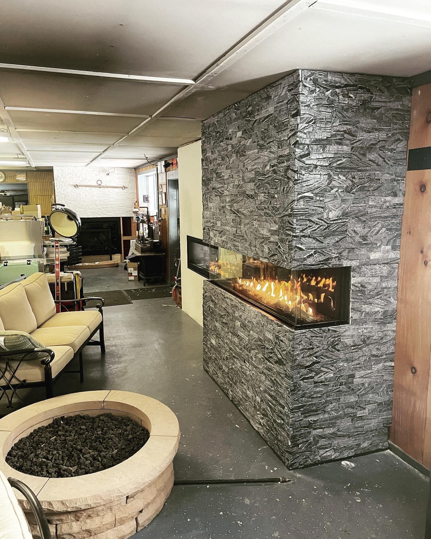 Stone fireplace with flames, concrete fire pit, and a sofa in a room.