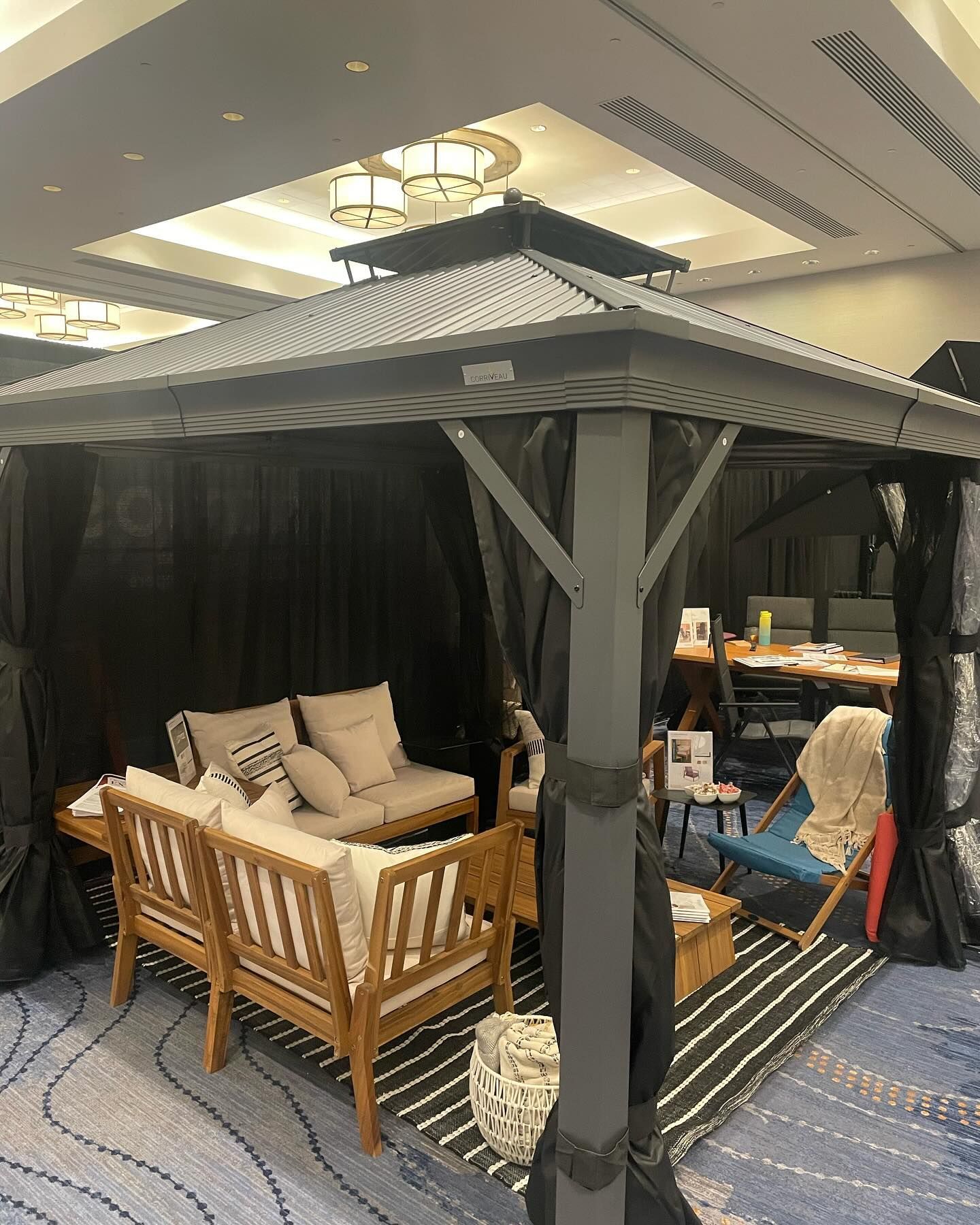 Gazebo with seating, black curtains, and striped rug indoors.