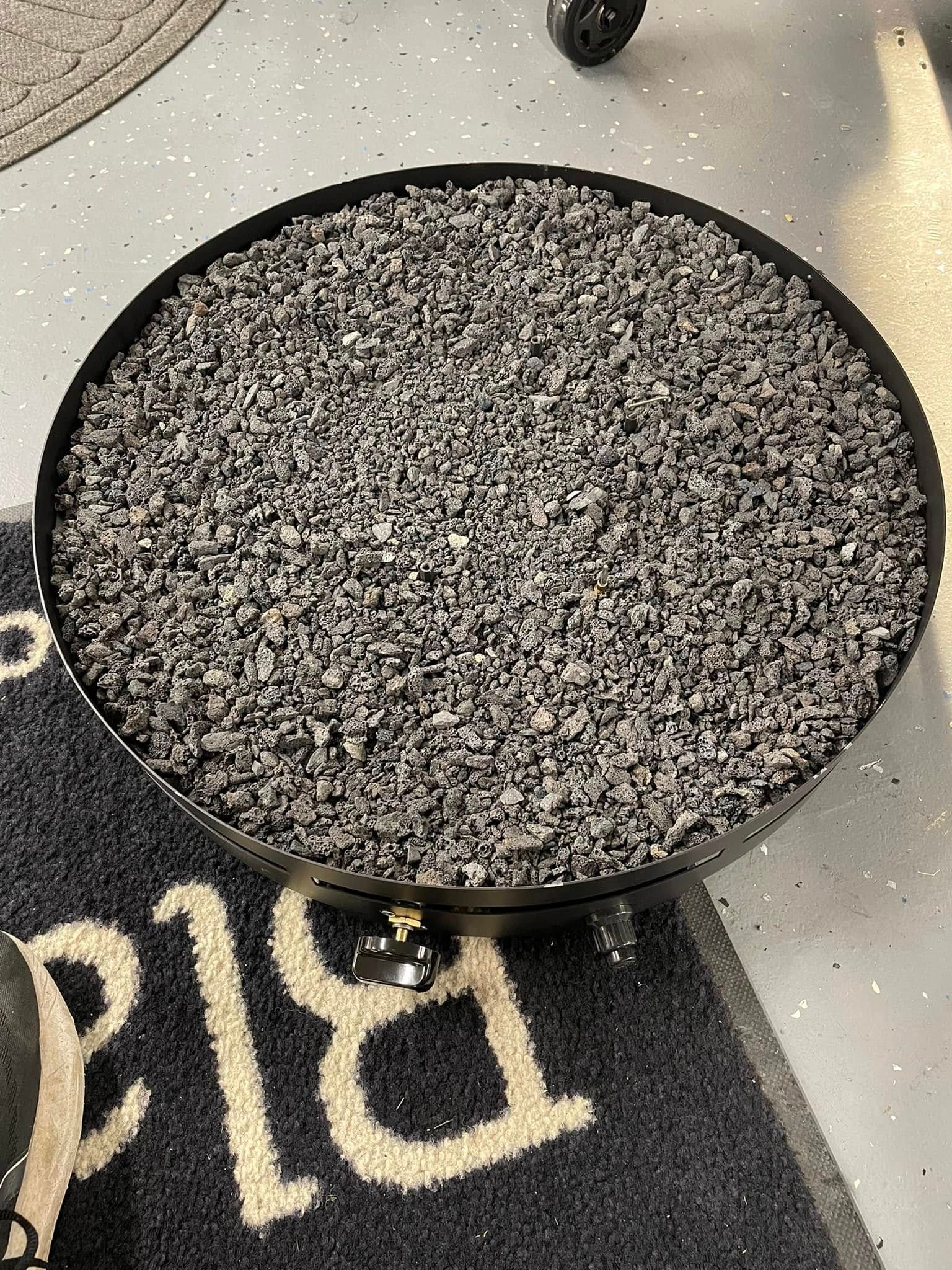 Black fire pit filled with gray lava rocks, resting on a blue doormat.
