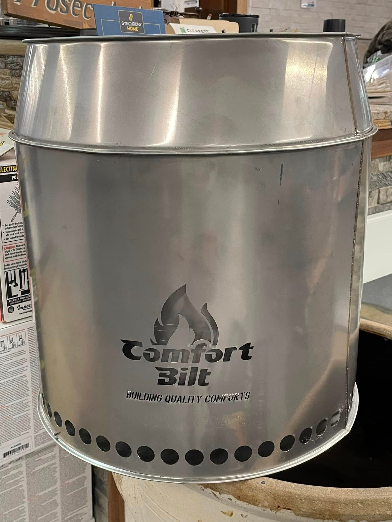 Silver Comfortbilt wood-burning barrel stove with flame logo, black vents around the bottom.