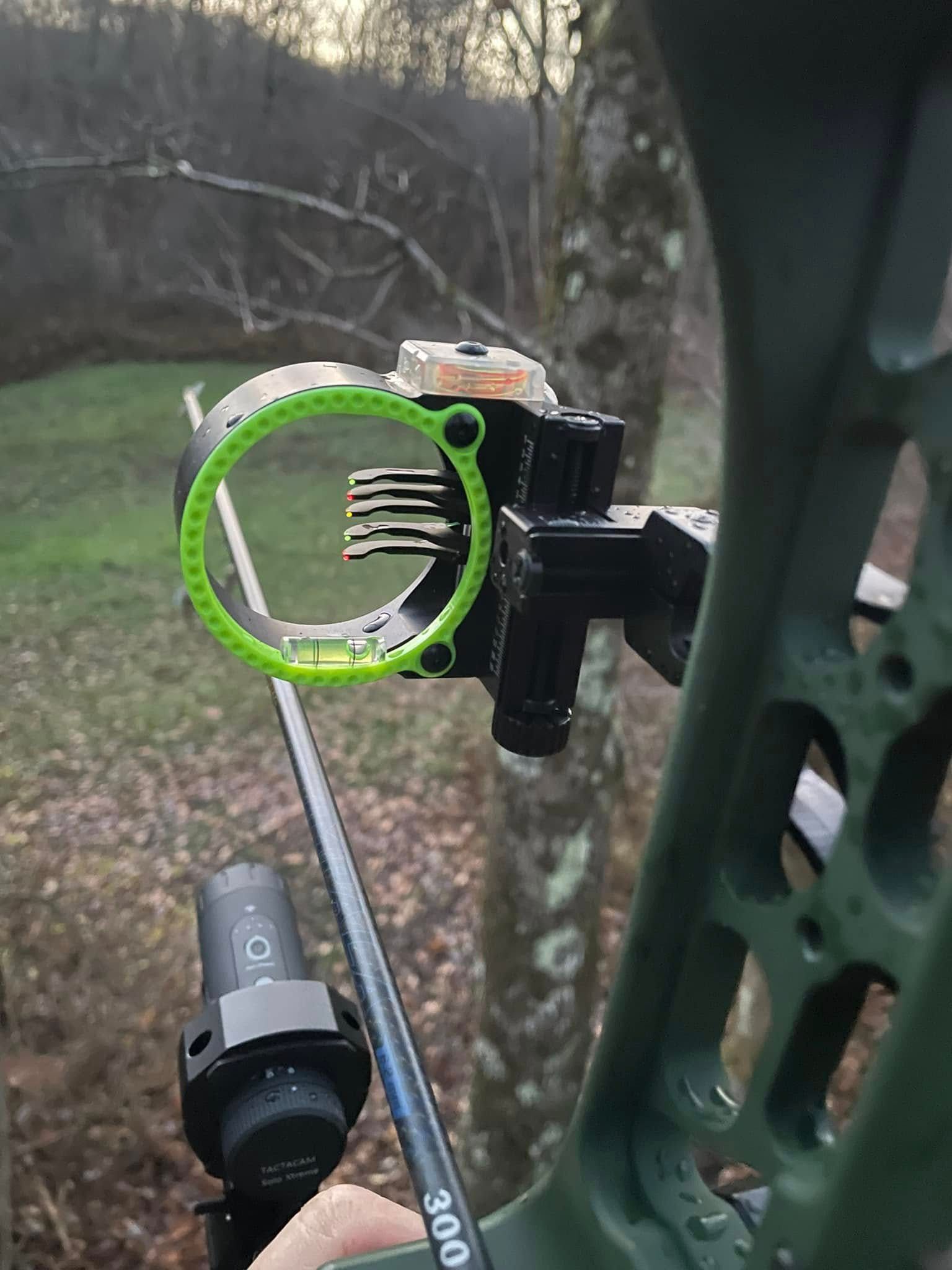 Green archery sight with level mounted on a bow, outdoors.
