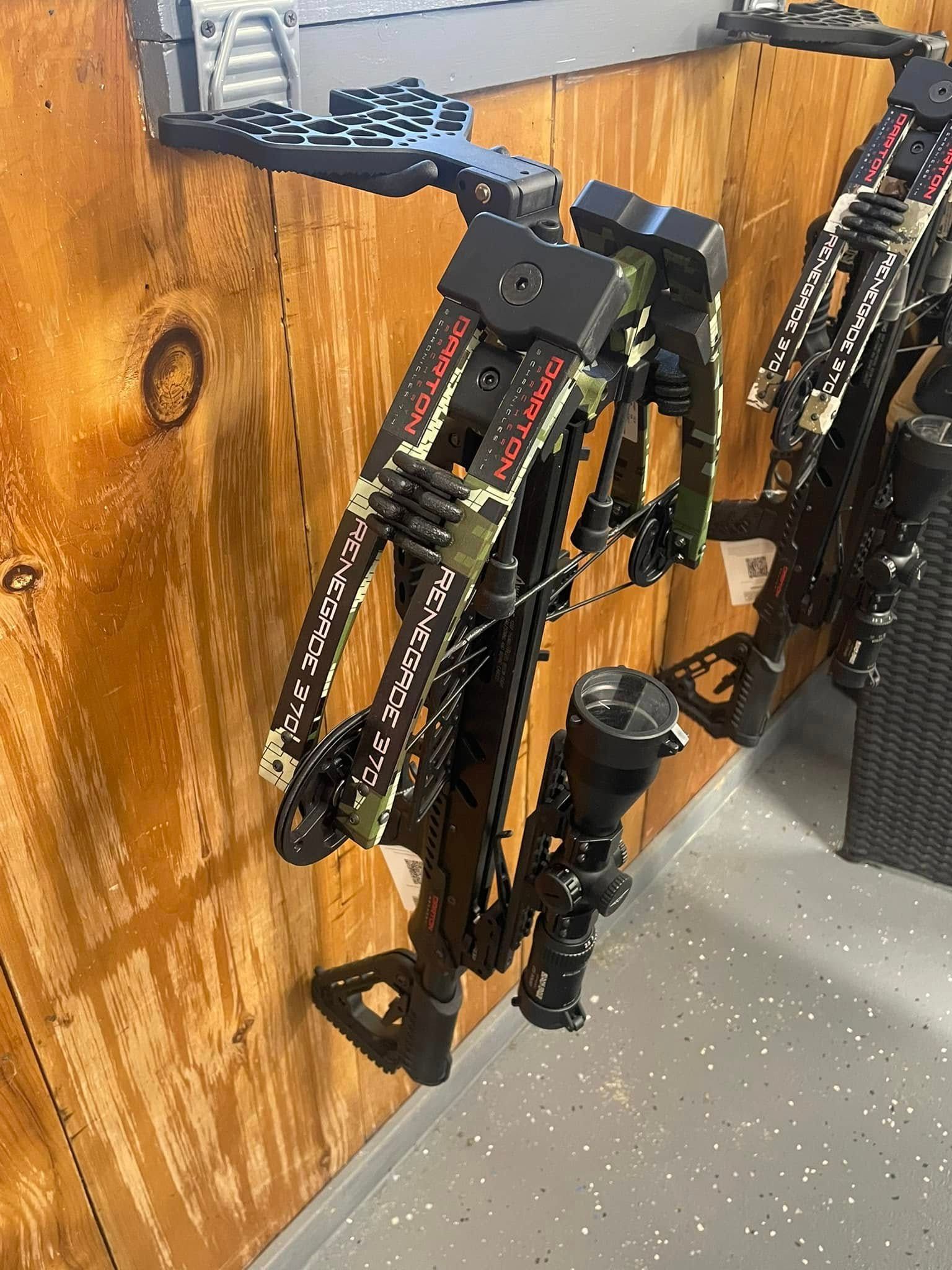 Crossbow hanging on a wooden wall, with camouflage design and scope attached.