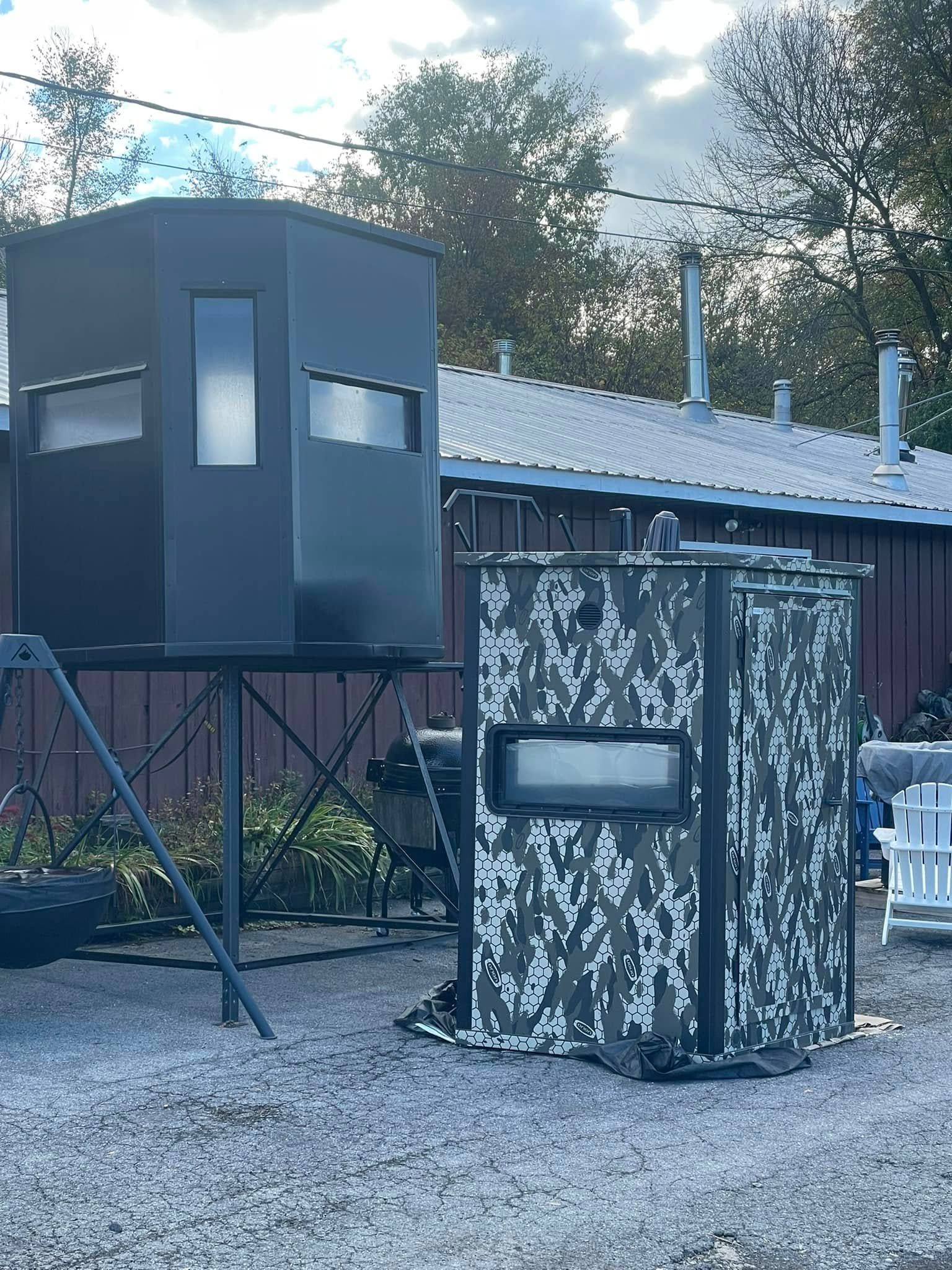 Two hunting blinds: one black, elevated, and one camouflage, ground-level, on a gravel surface.
