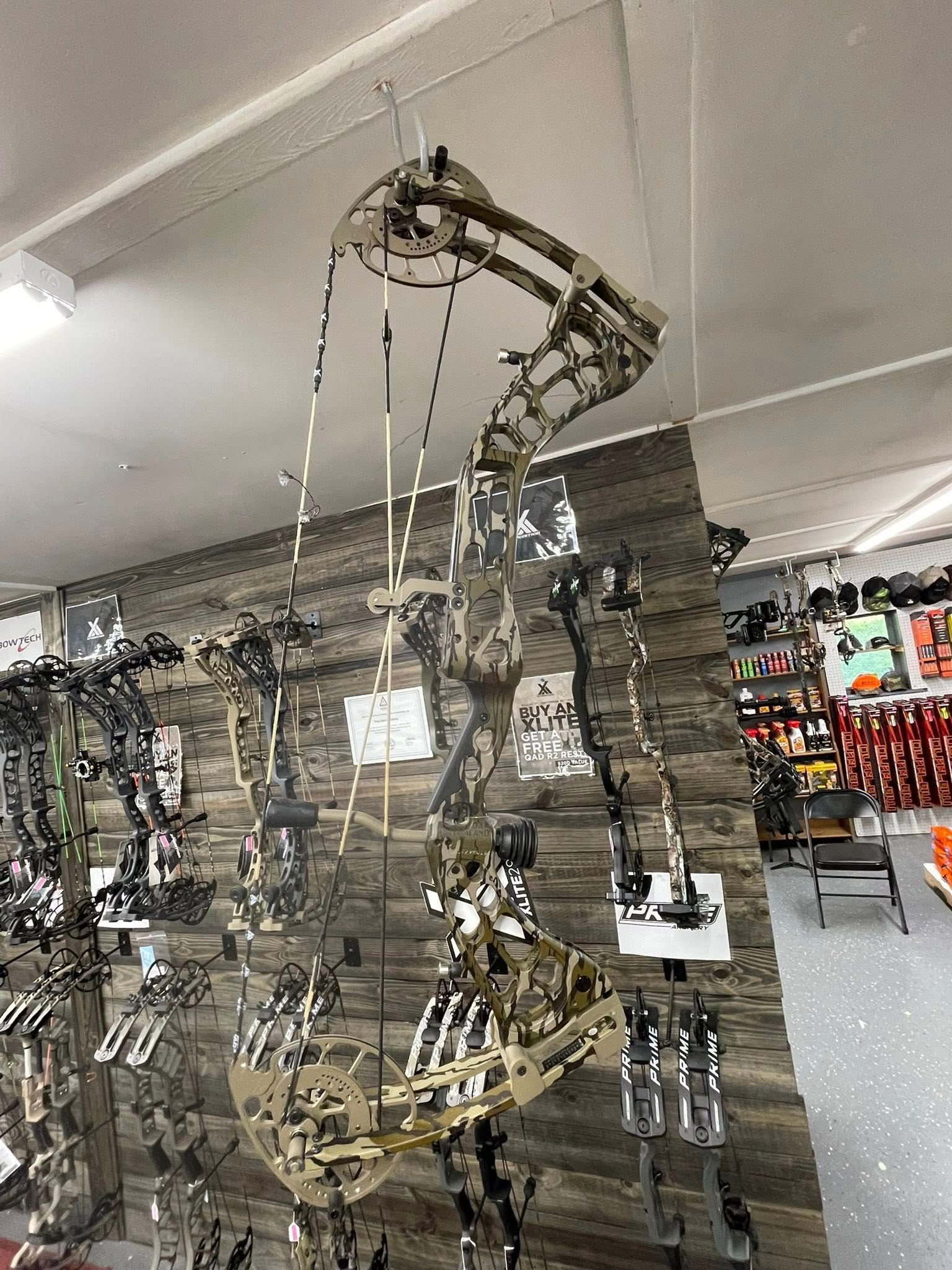 Compound bow hanging in a store, brown and beige colors, attached to a wooden wall.