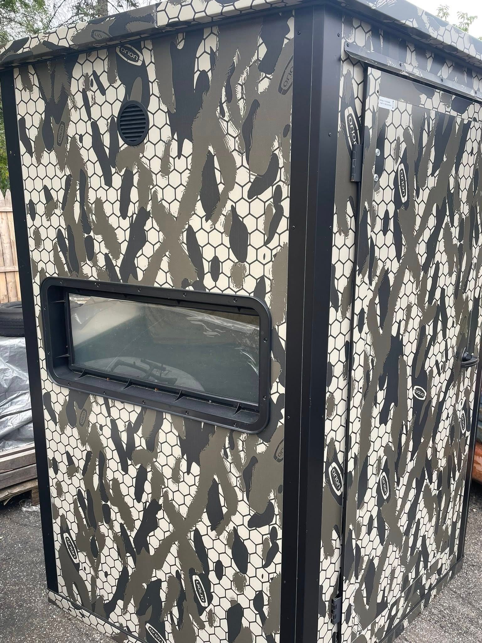 Camouflage hunting blind with window and black trim.